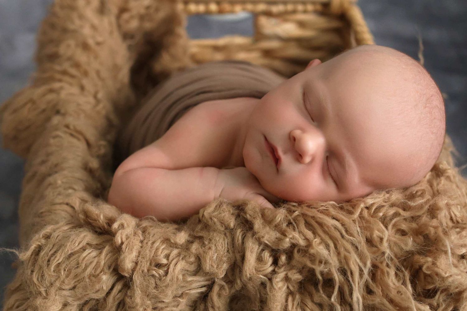 Sleeping newborn baby resting peacefully on soft brown textured blanket.