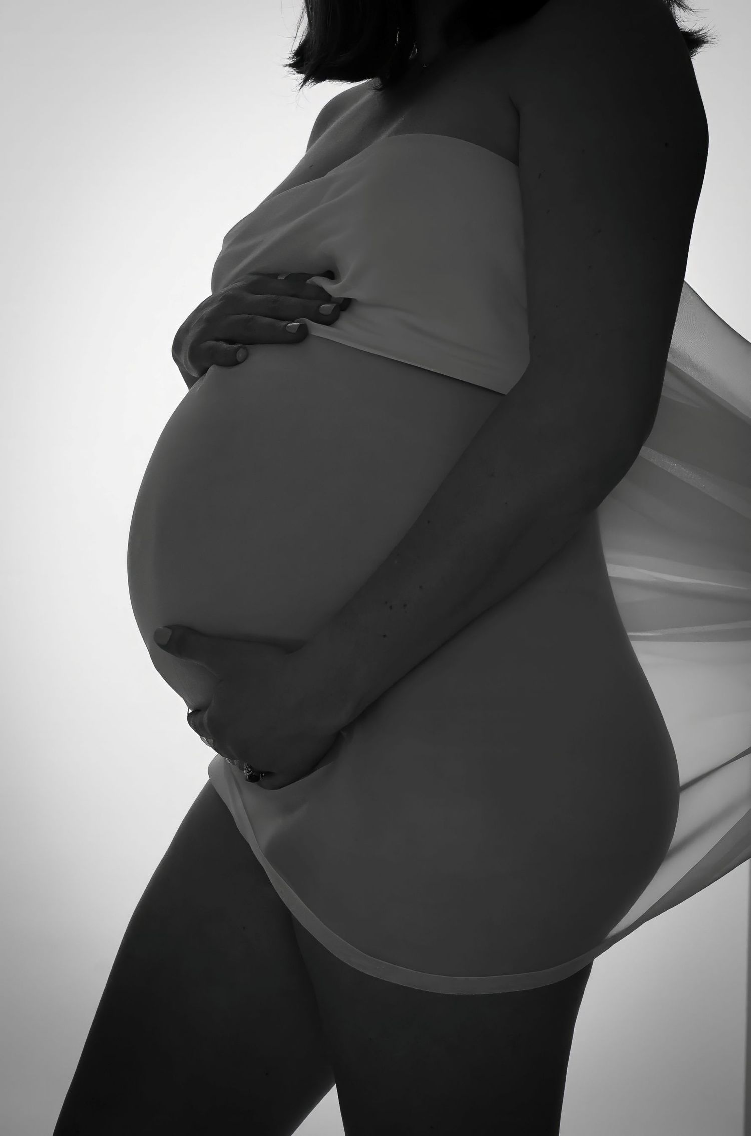 Black and white silhouette of a pregnant figure in intimate maternity wear against light background.