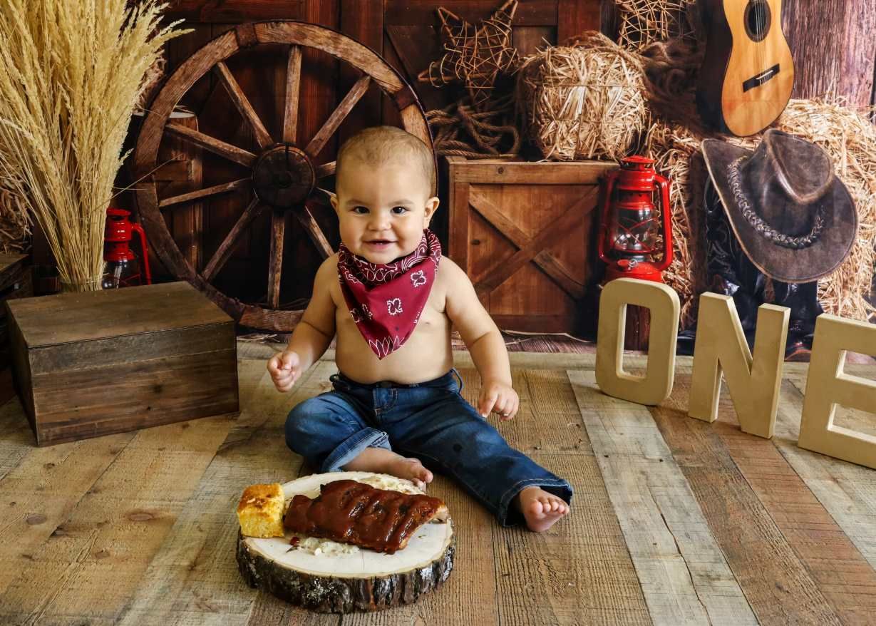 A rustic western-themed birthday setup with a smash cake on wooden floor surrounded by wagon wheel and guitar decor.