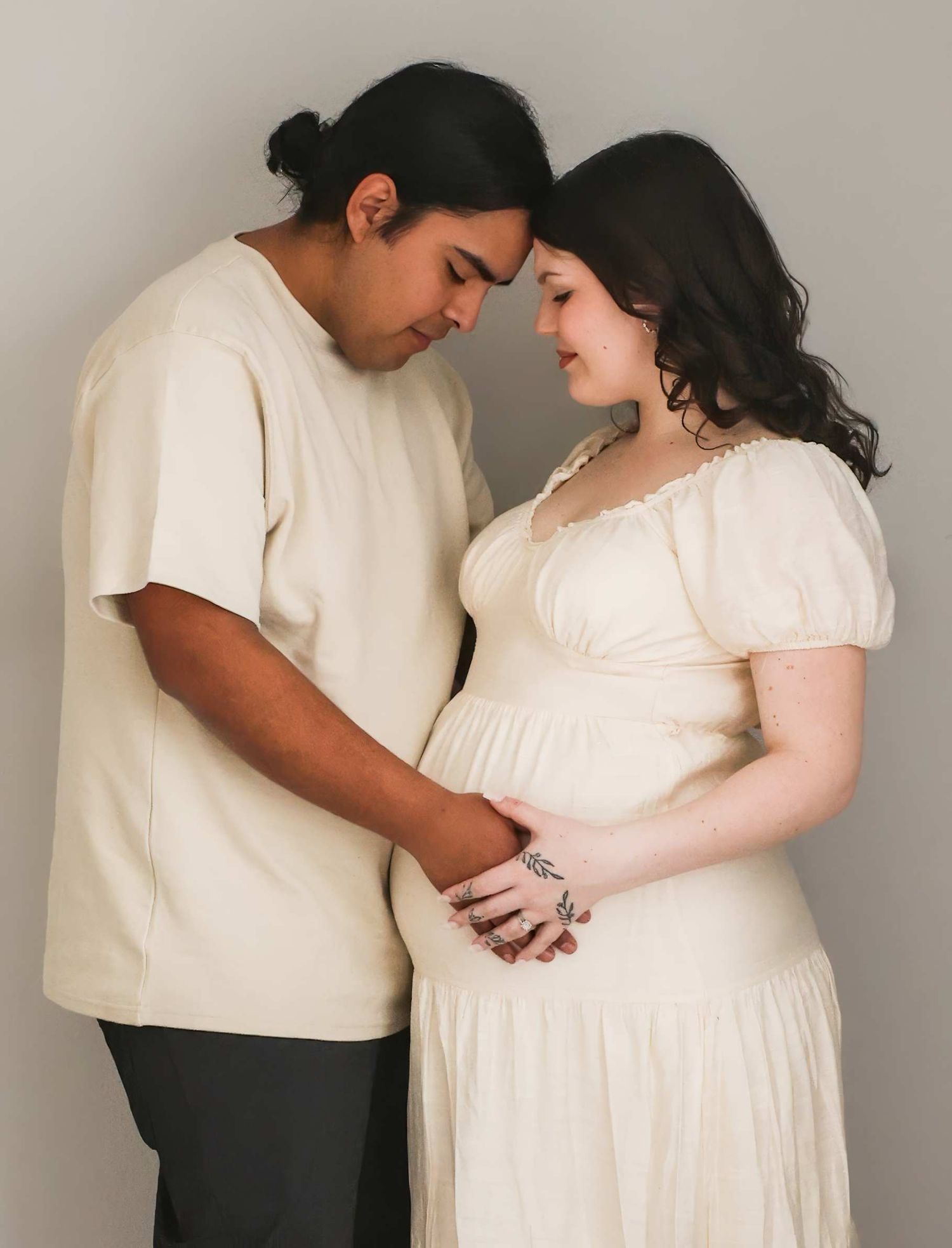 Intimate maternity portrait of couple in white clothing sharing tender moment together.