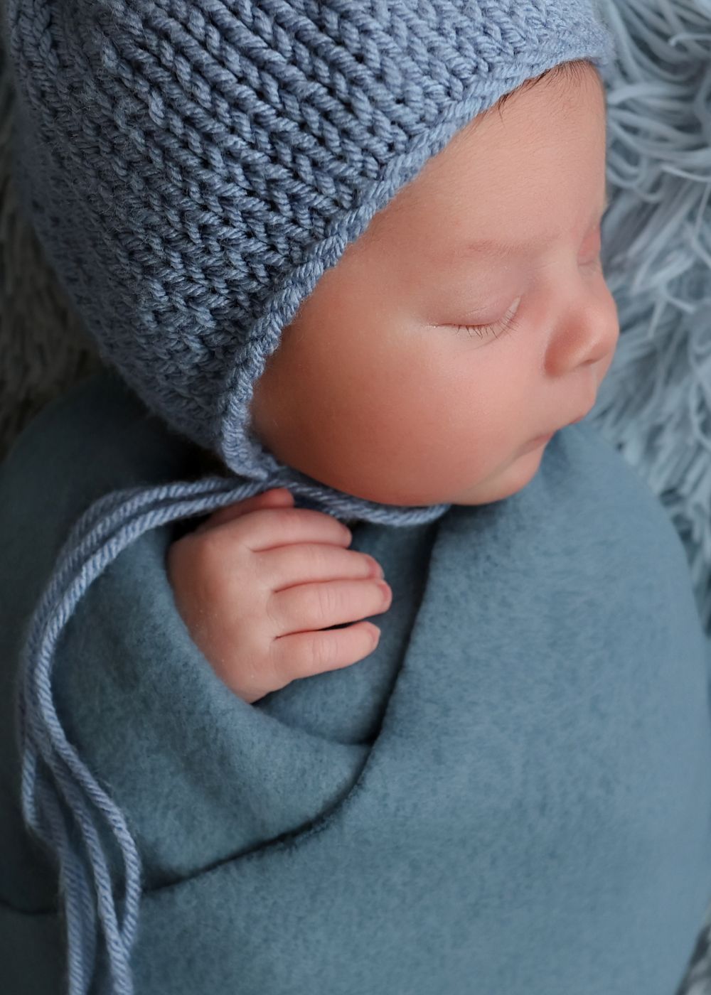 Sleeping newborn baby wrapped in soft blue blanket wearing a knitted blue bonnet hat.