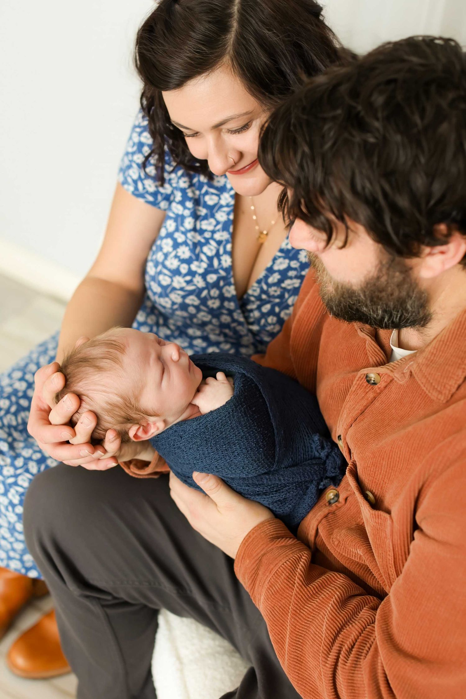 A parent in a brown sweater holds and comforts a small baby wearing a navy blue outfit.
