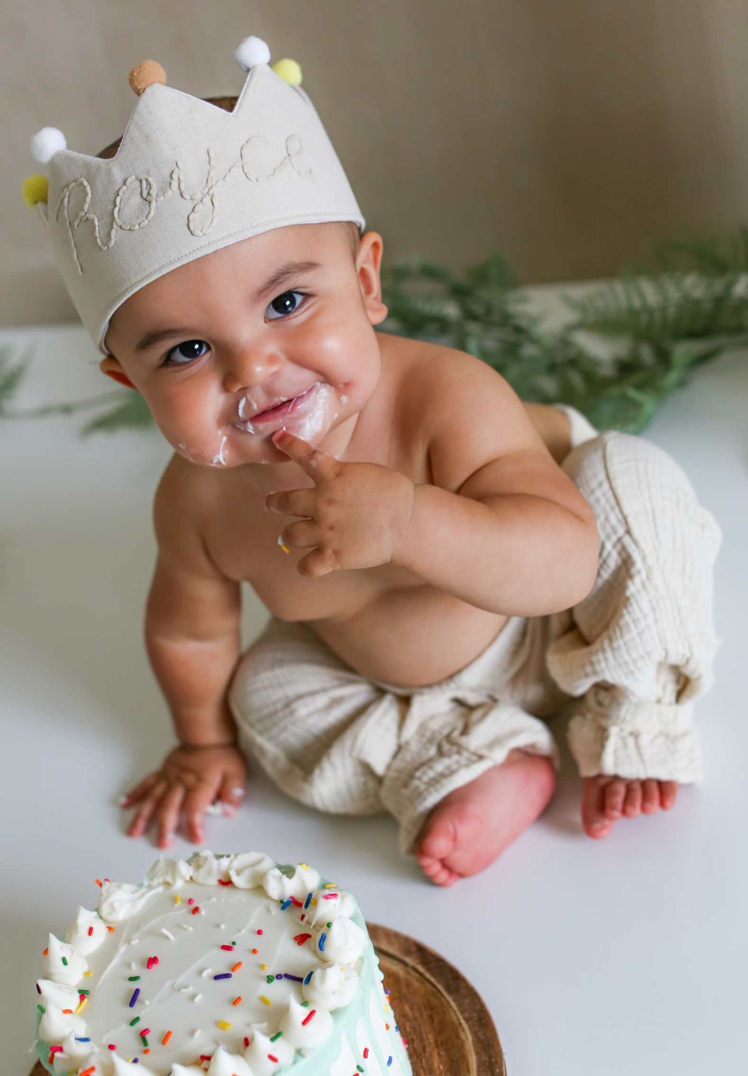 A cake smash celebration with a white frosted cake and a small crown-wearing participant.