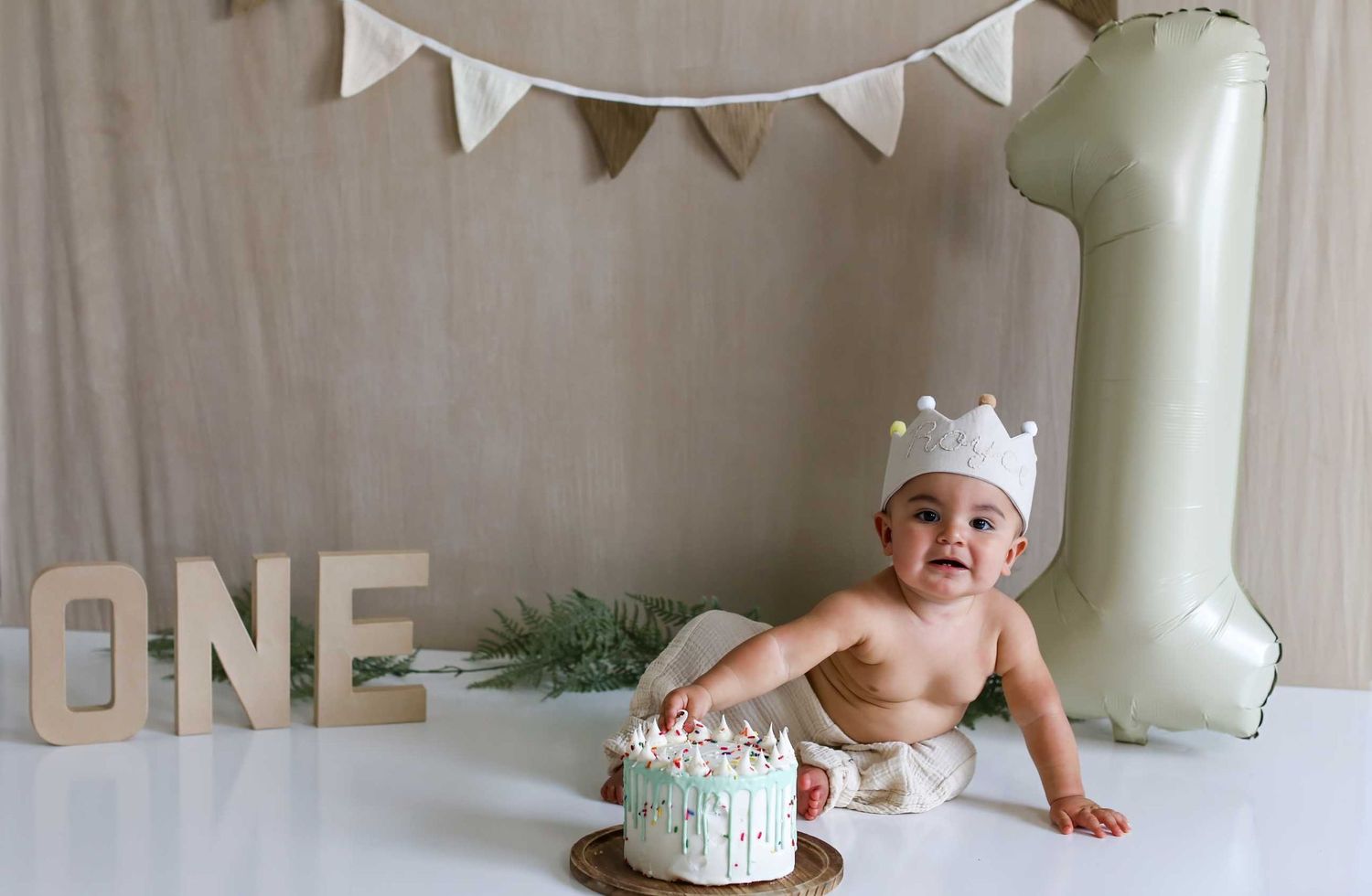 A baby's first birthday celebration with white bunting decorations and a smash cake setup.