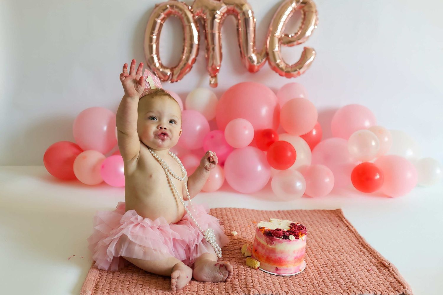 Birthday photoshoot with pink balloon arch and 'ONE' text balloons in rose gold.
