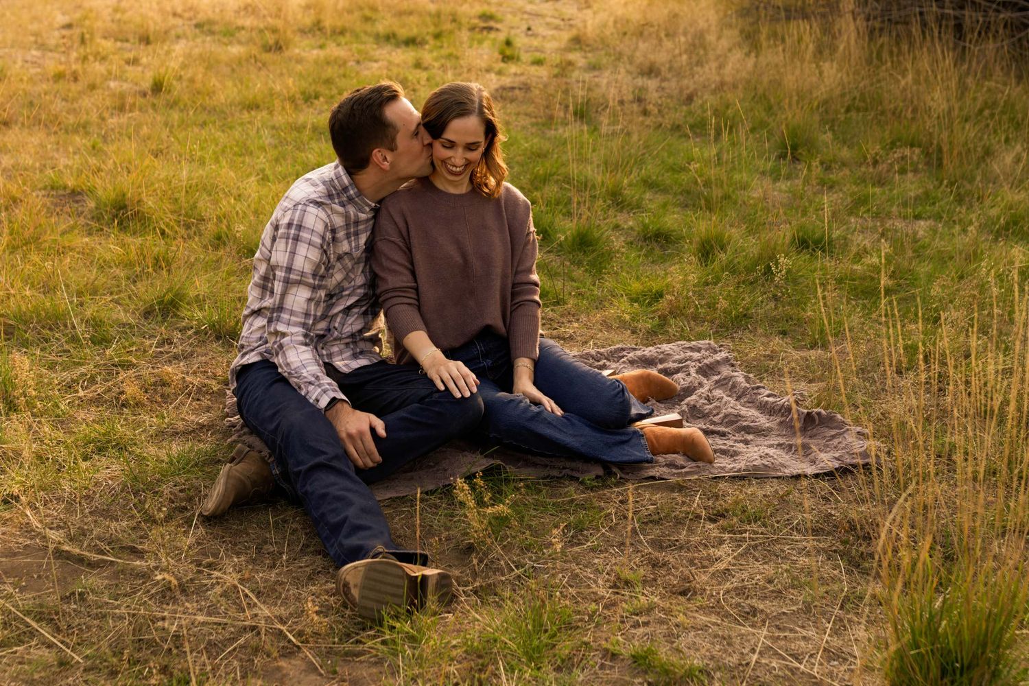 A couple shares an intimate moment while sitting together in a golden autumn field at sunset.