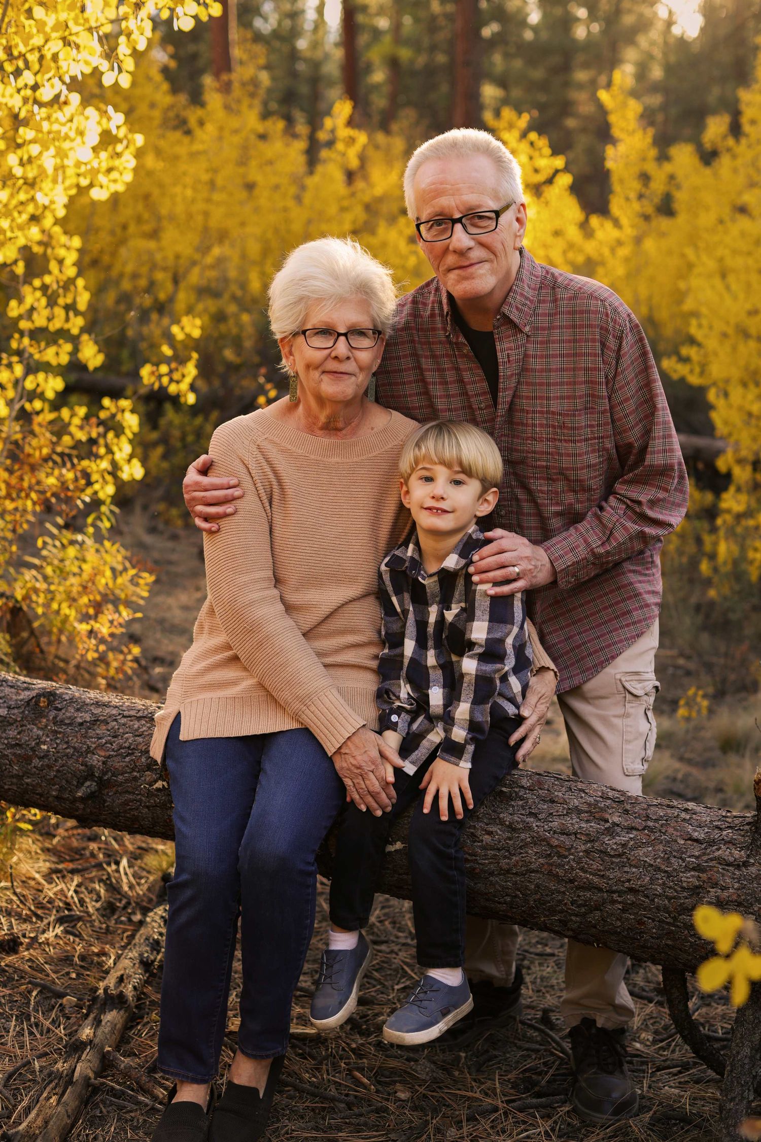 Family sits together on fallen log surrounded by golden autumn foliage during outdoor photo session.