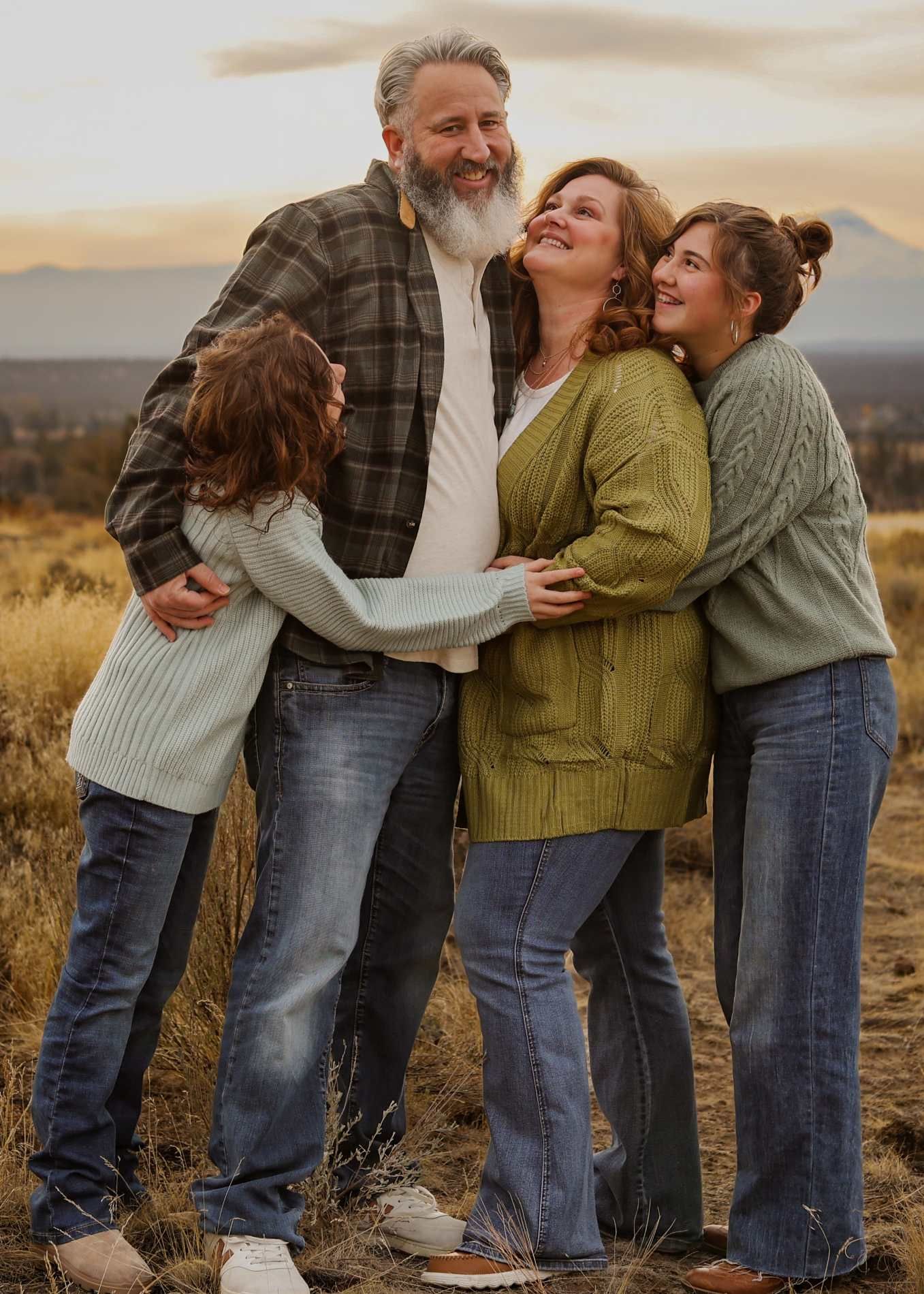 Family sharing a joyful embrace while wearing cozy sweaters in a golden field at sunset.