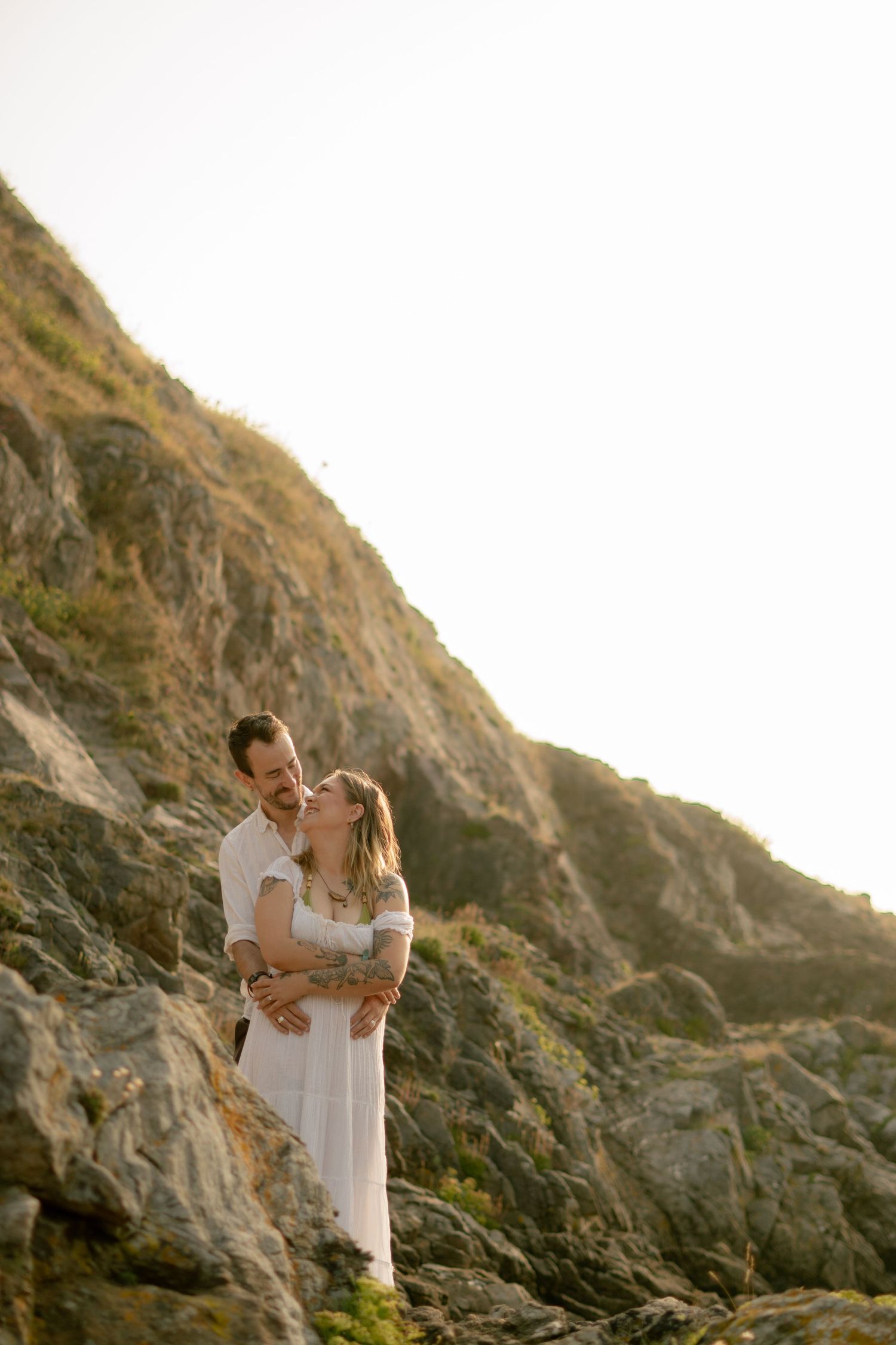 A man cuddling his pregnant fiancé on the beach at Churston Cove, Devon.