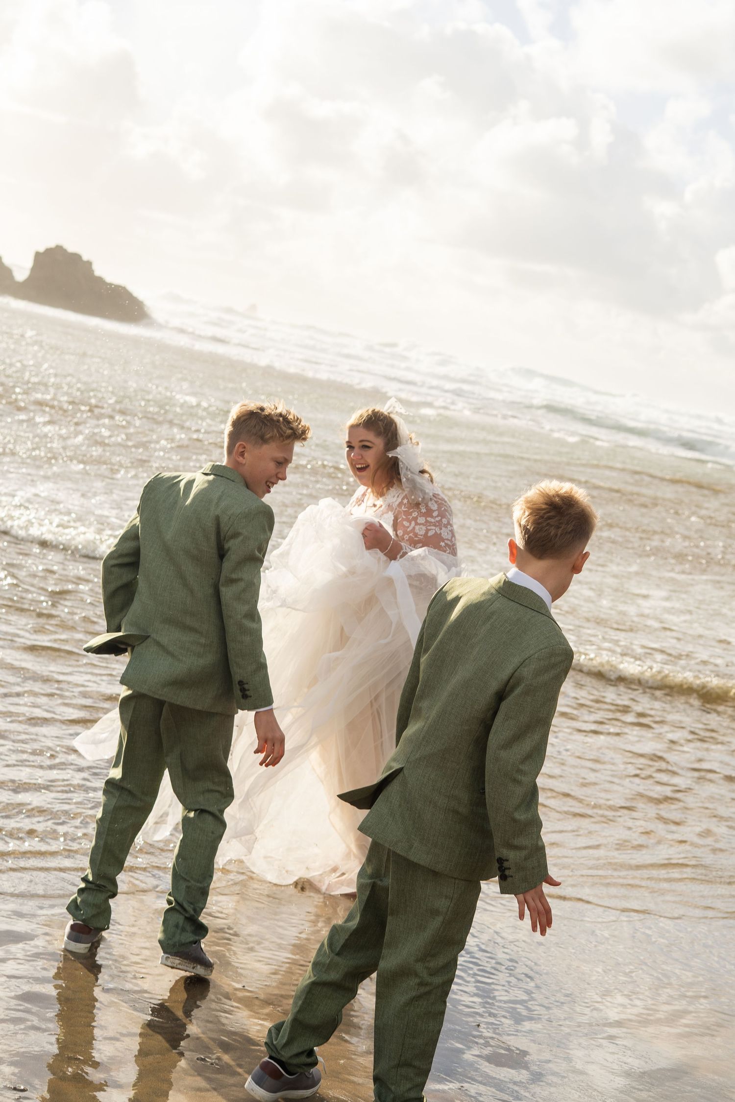 A bride playing in the sea and laughing with her two sons on Perranporth beach, after her wedding ceremony in Truro, Cornwall.
