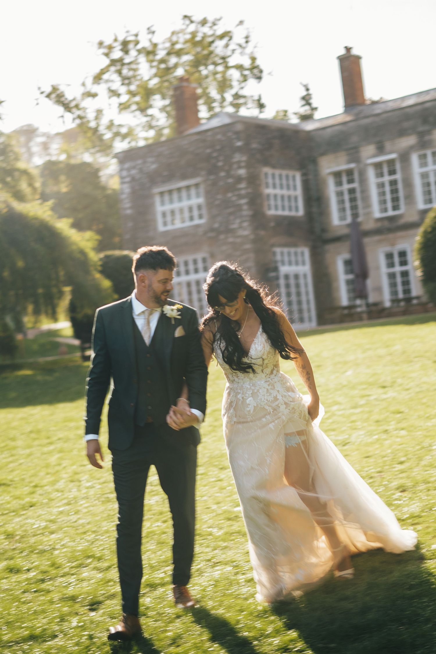 A motion blur photo of bride and groom walking outside of Cockington Court, Torquay, Devon, with natural green lighting during golden hour.