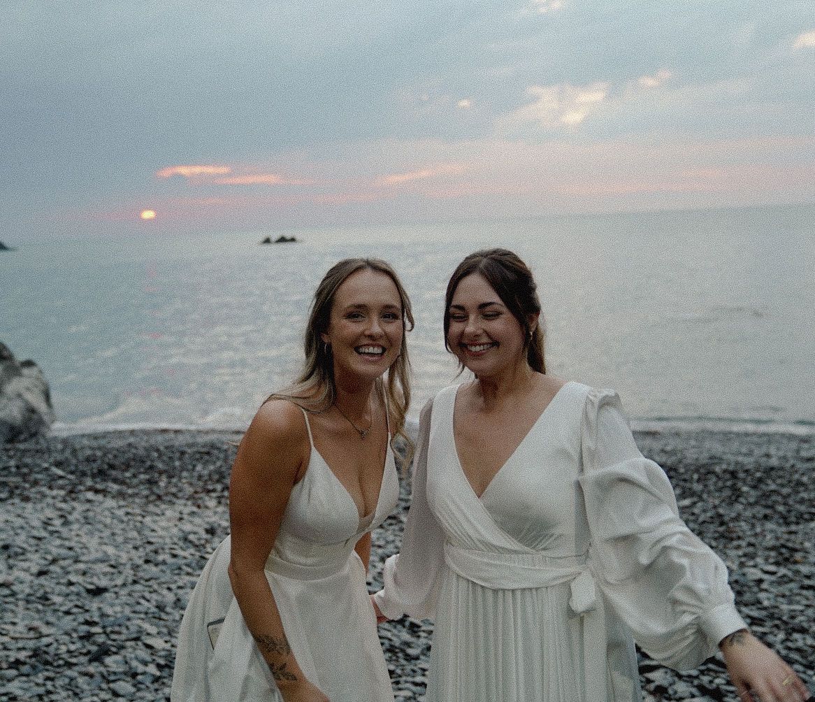 Wives smiling together at sunset on their wedding day at Tunnels Beaches, Ilfracombe, Devon.