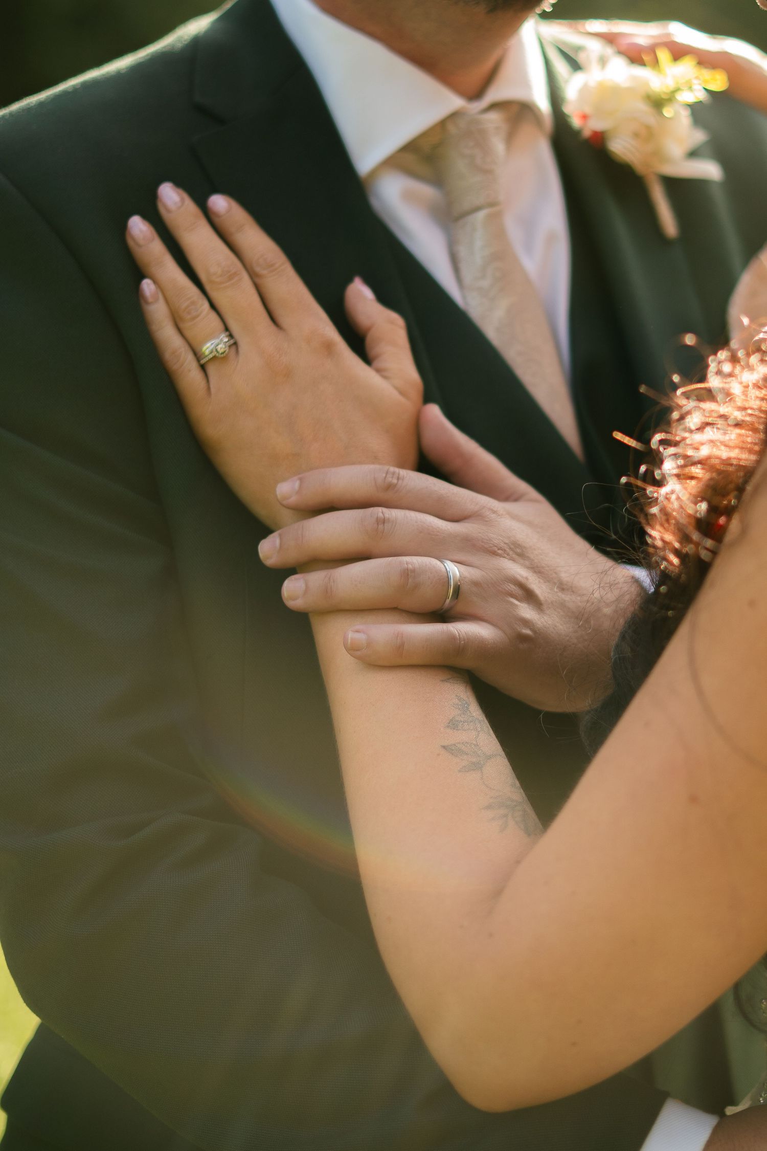 A bride resting her hand on the groom's chest, with his hand over the top, showing both wedding rings.