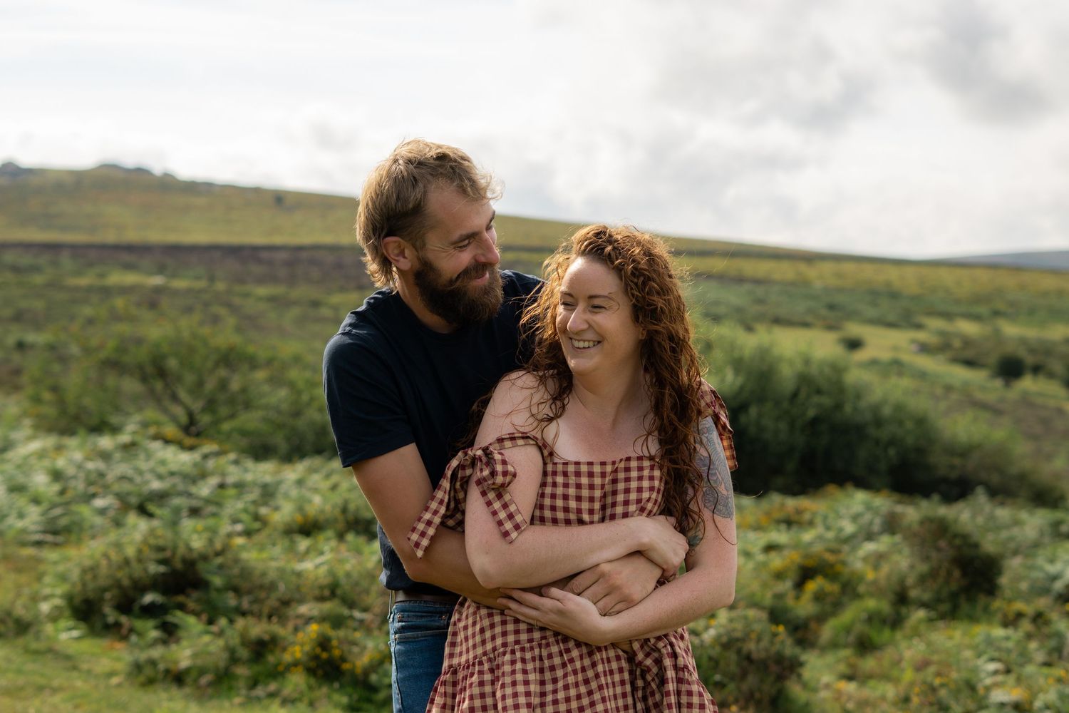 A man cuddling his fiancé from behind at Dartmoor National Park, Devon, England, whilst both giggling.