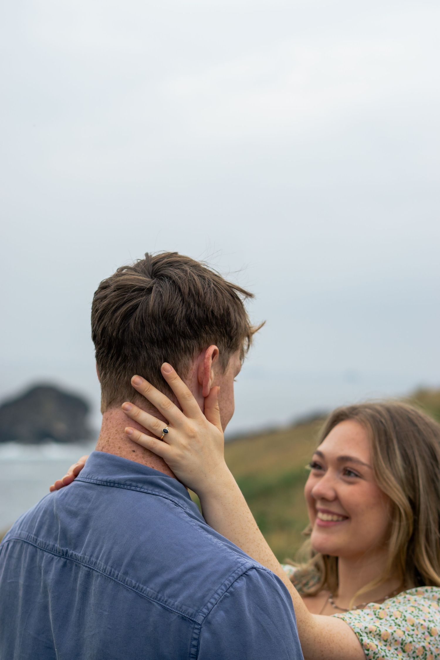 A woman holds her fiancé's face for a kiss on the clifftop at Park Head near Porthcothan Bay in Cornwall.