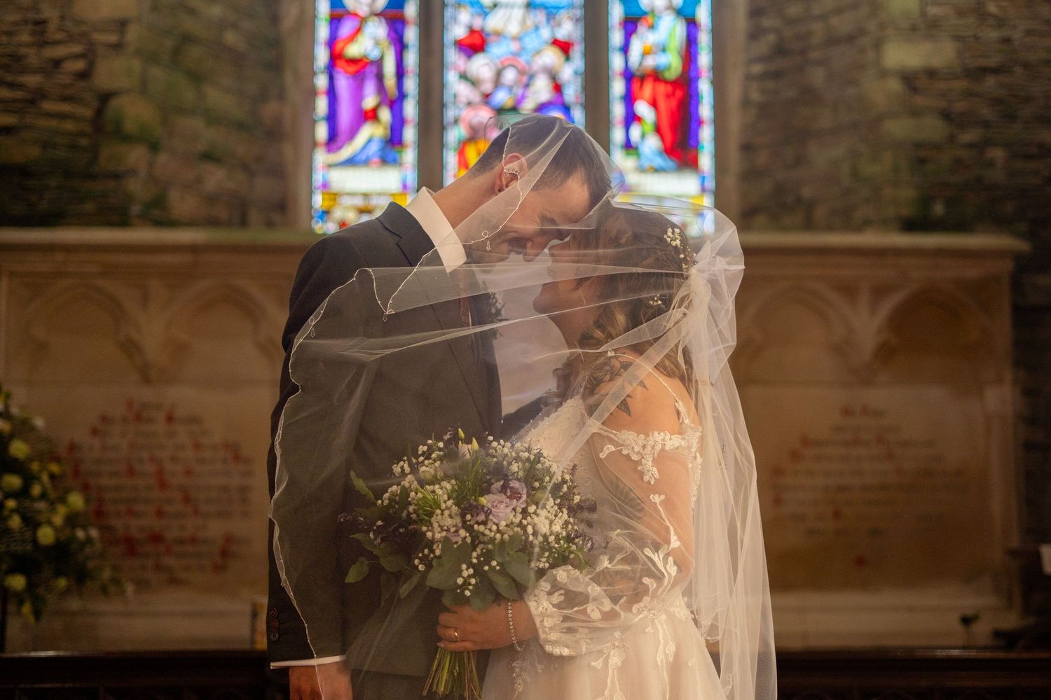 The bride and groom smiling together under the veil, during their church wedding ceremony in Berrynarbor, North Devon.