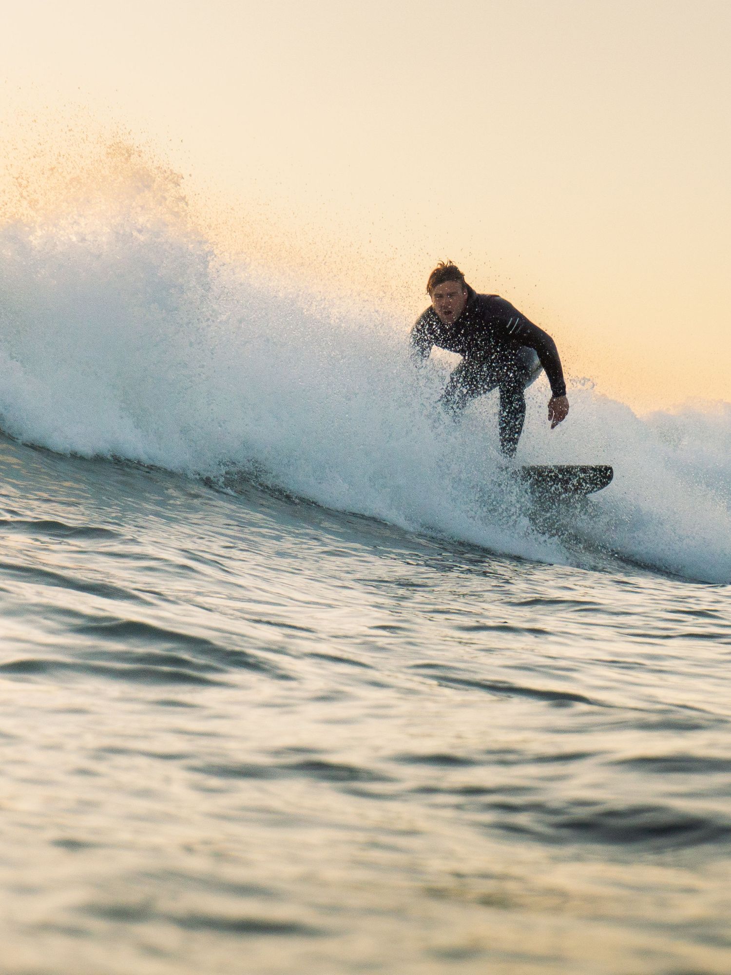 An in-water photo of a surfer riding a wave at Bantham Beach, Devon during sunset.
