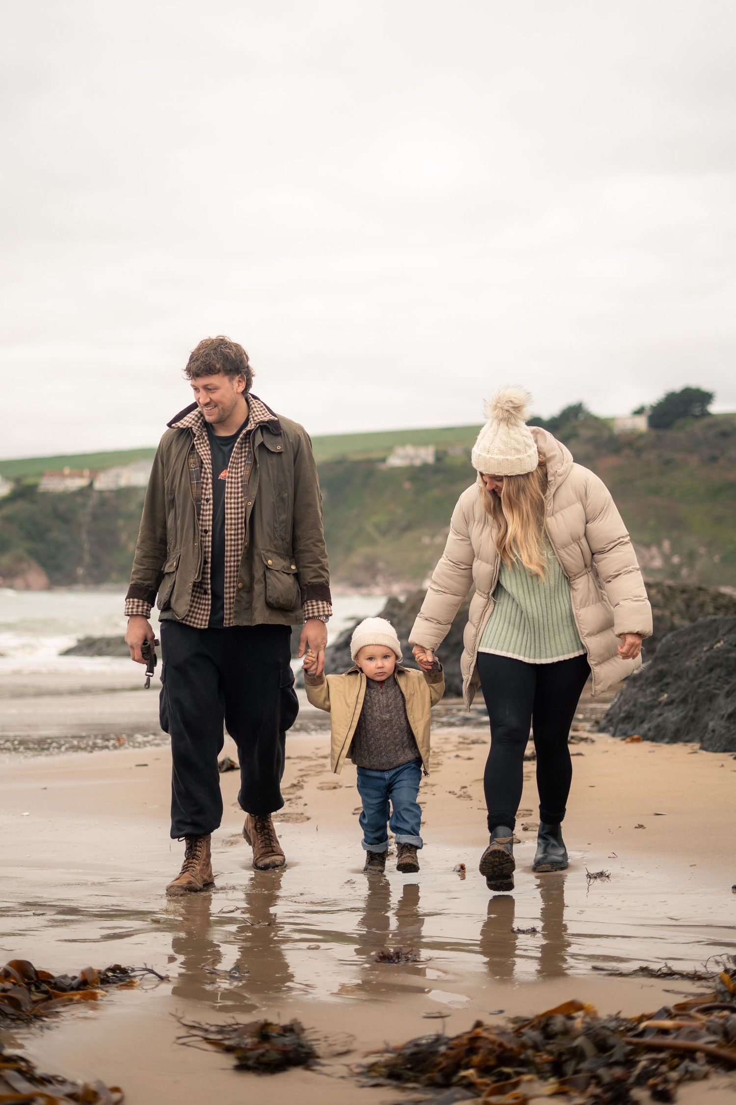 A young family hold hands, walking on Bantham Beach, South Devon, during a family photoshoot.