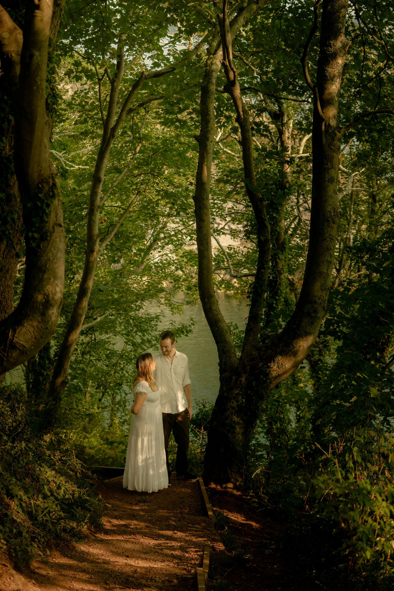 A couple walking in the forest with a pale sunlight backdrop at Churston Cove, Devon.