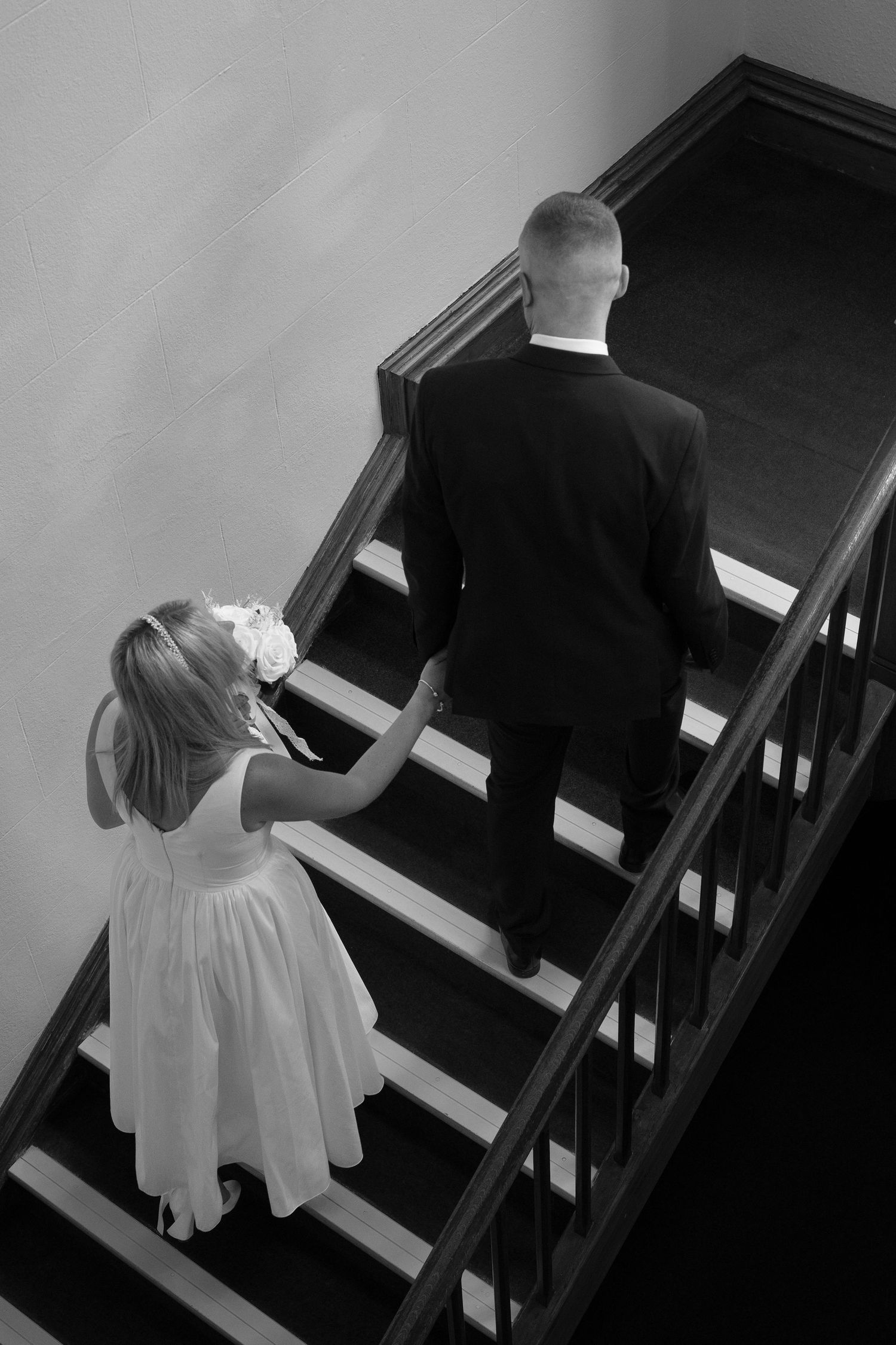 The bride and groom walking up stairs, hand-in-hand at Liskeard Registration Office, Cornwall.