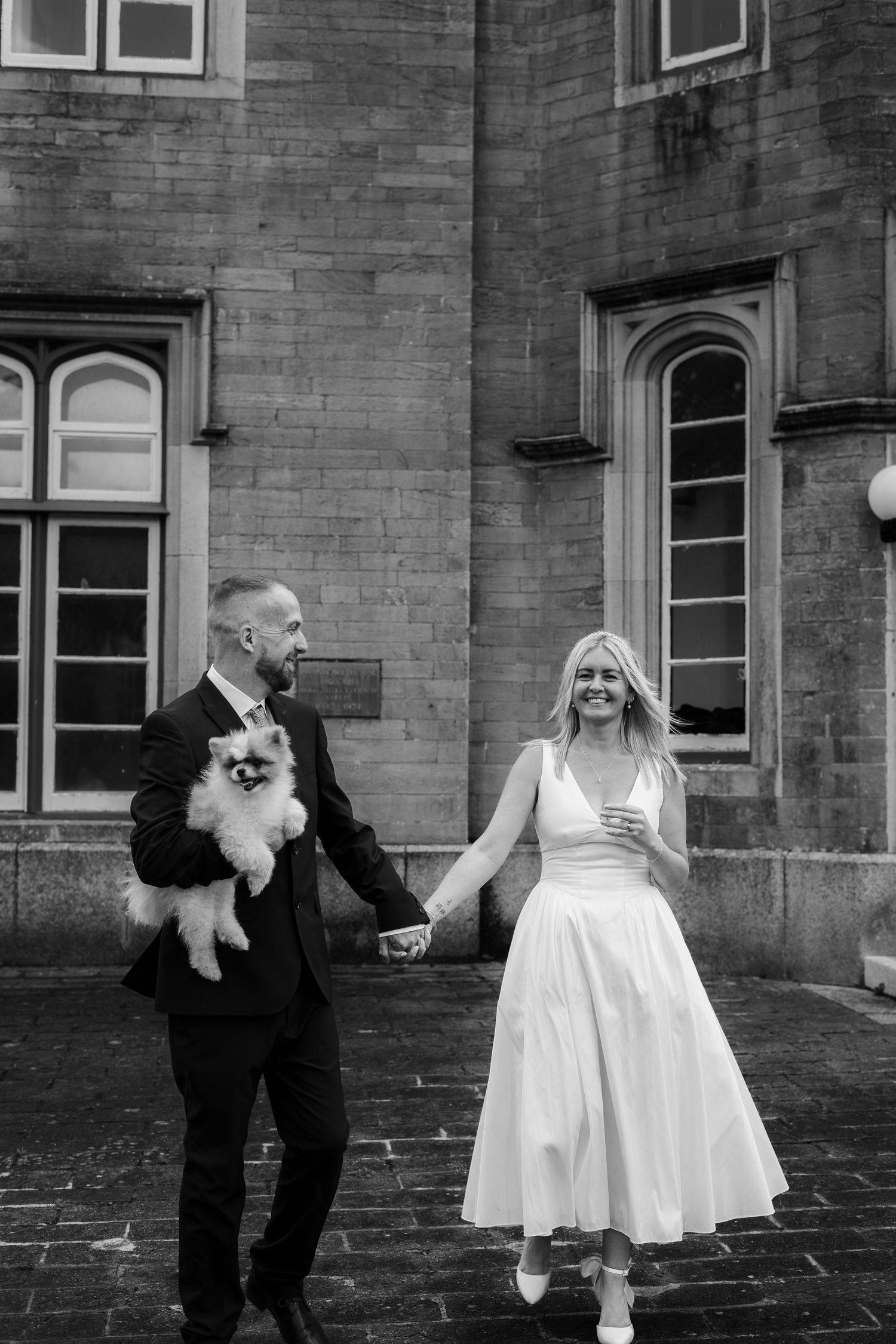 A bride and groom walking hand in hand, with their dog at Liskeard Registration Office, Cornwall.