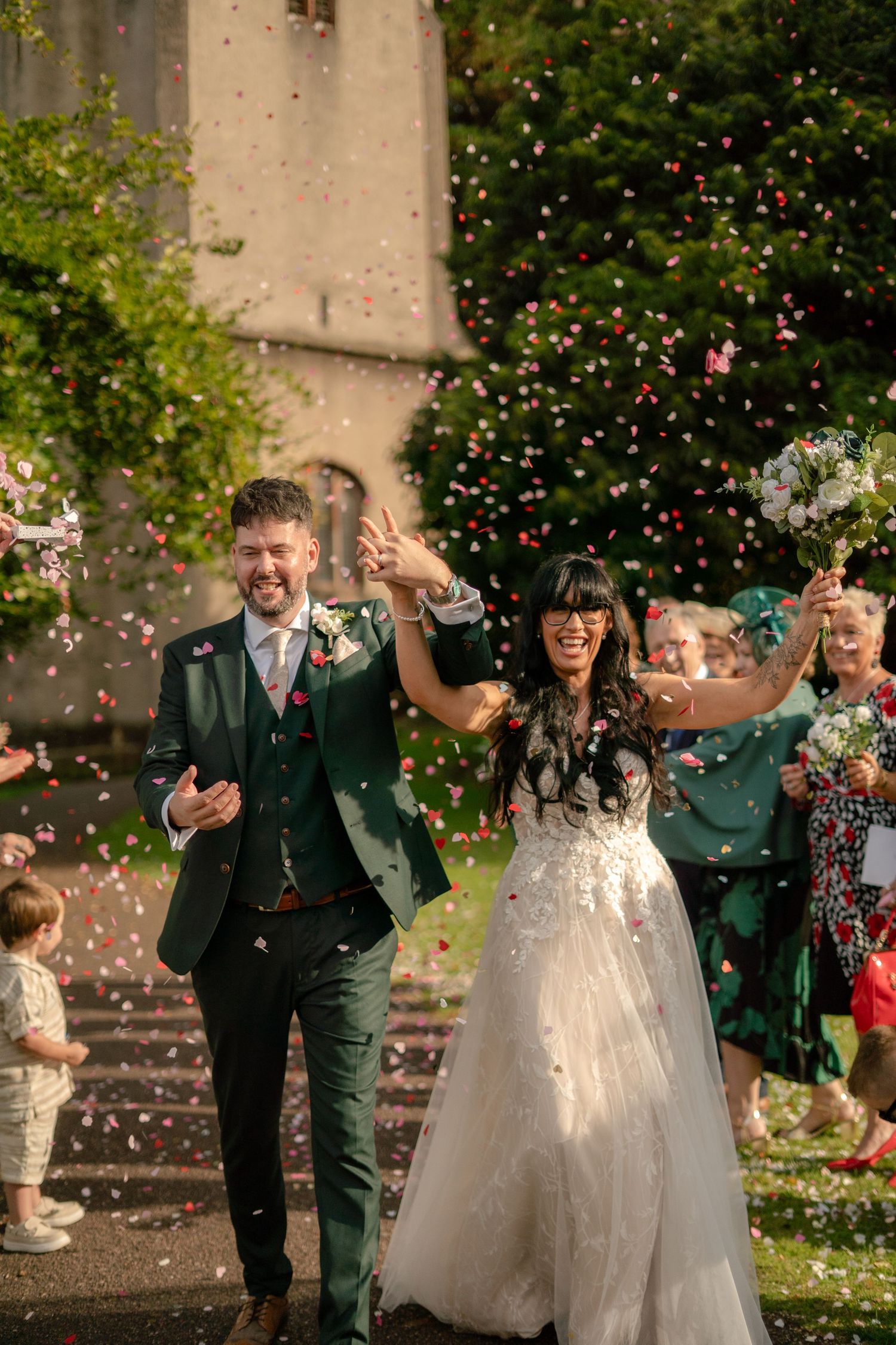 Bride and groom walking through confetti after their wedding ceremony at Cockington Court, Torquay, Devon.