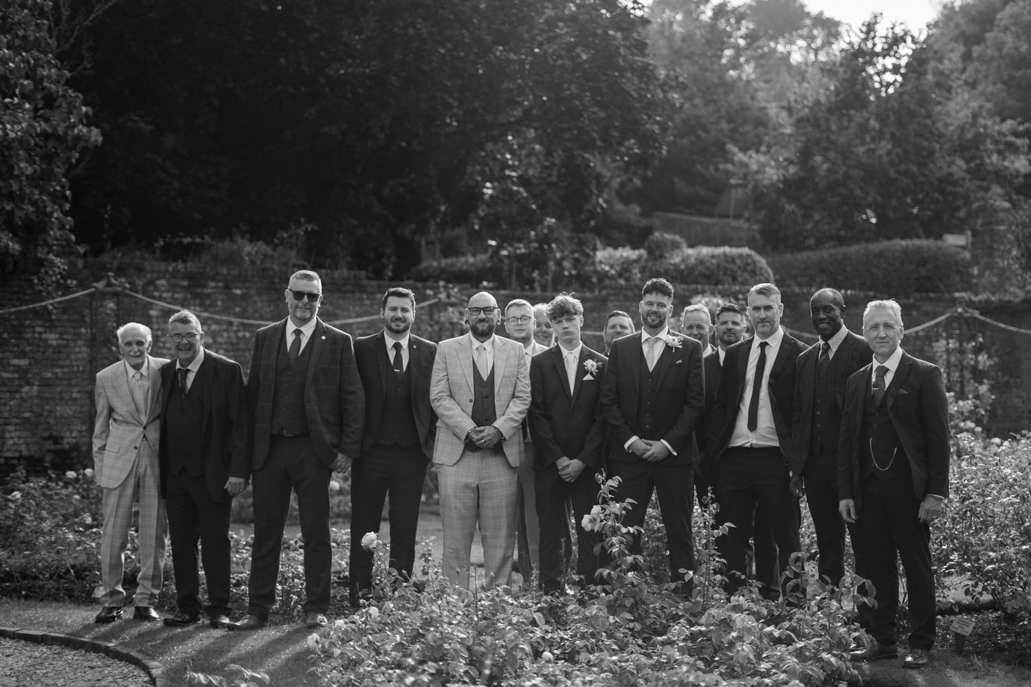 A large group photo of the groomsmen in the Cockington Court rose garden.
