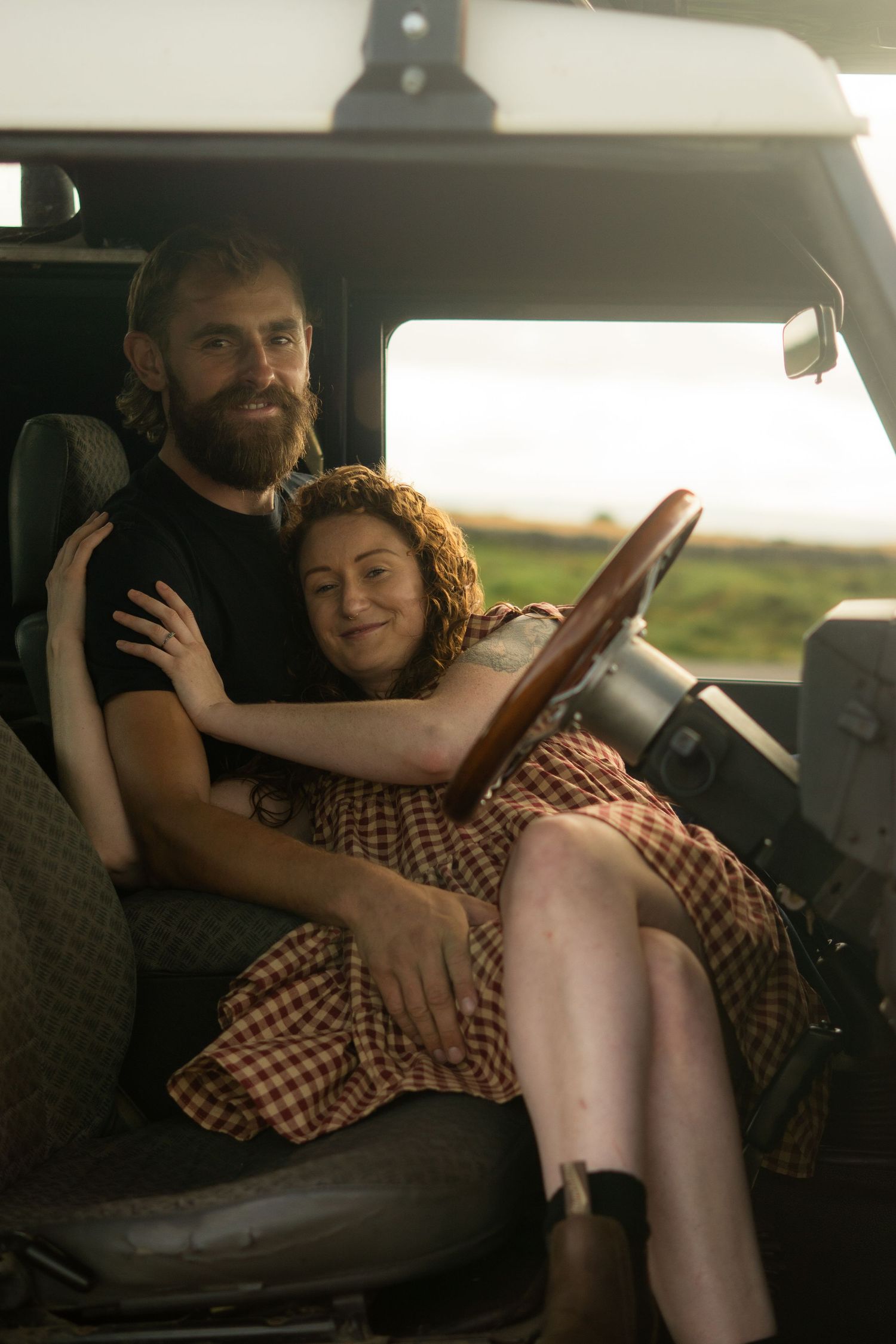 A man sitting in his land rover, with his fiancé laying back into him and cuddling at Dartmoor, Devon