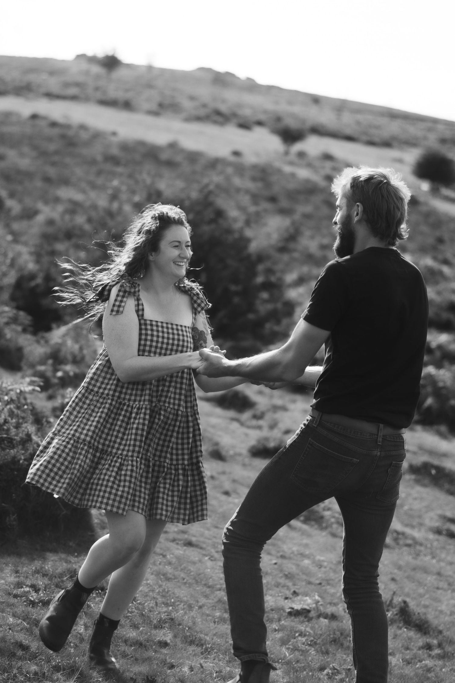 A black and white photo of a couple spinning and laughing on Dartmoor National Park, Devon.