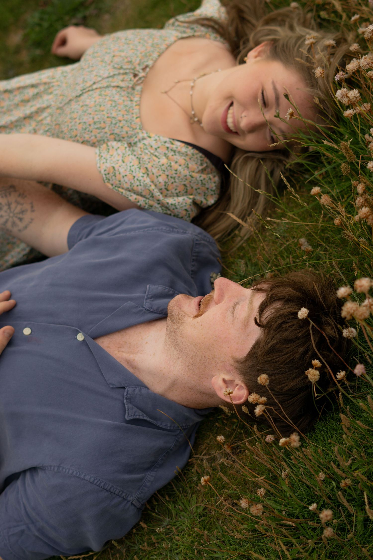 An engaged couple lay in an open field, looking into each other's eyes on an autumnal evening in Cornwall, UK.