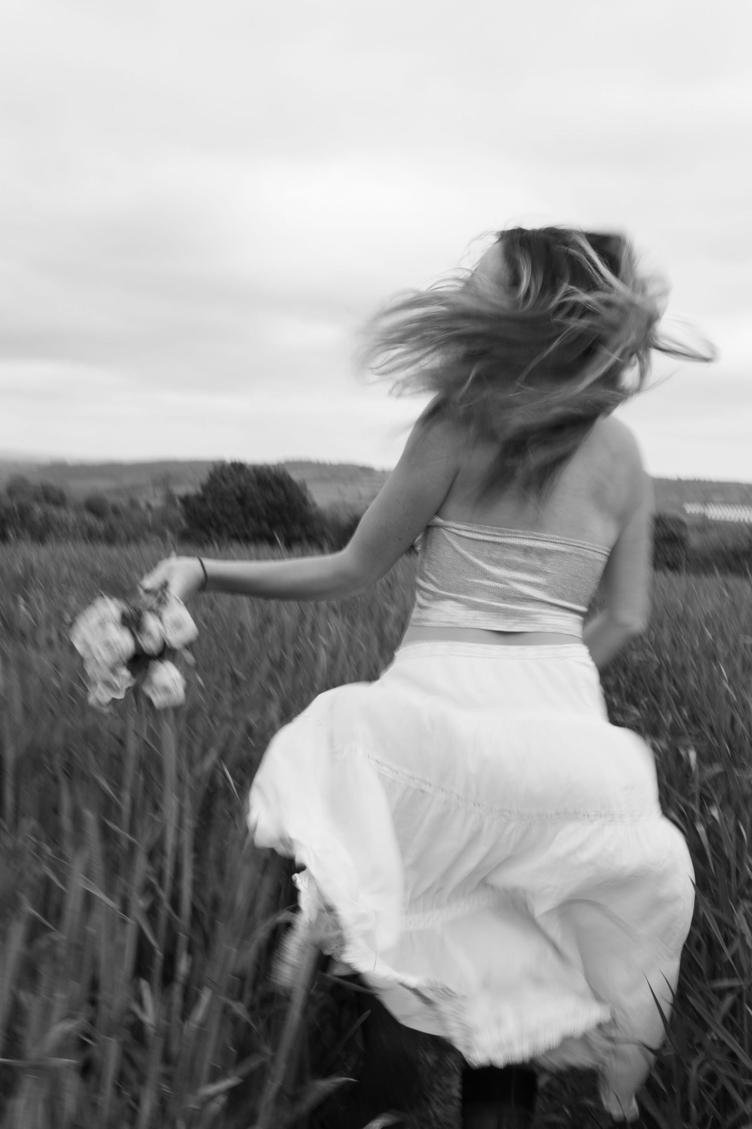 A black and white motion blur photo of a girl running through a Cornish field, bouquet in hand