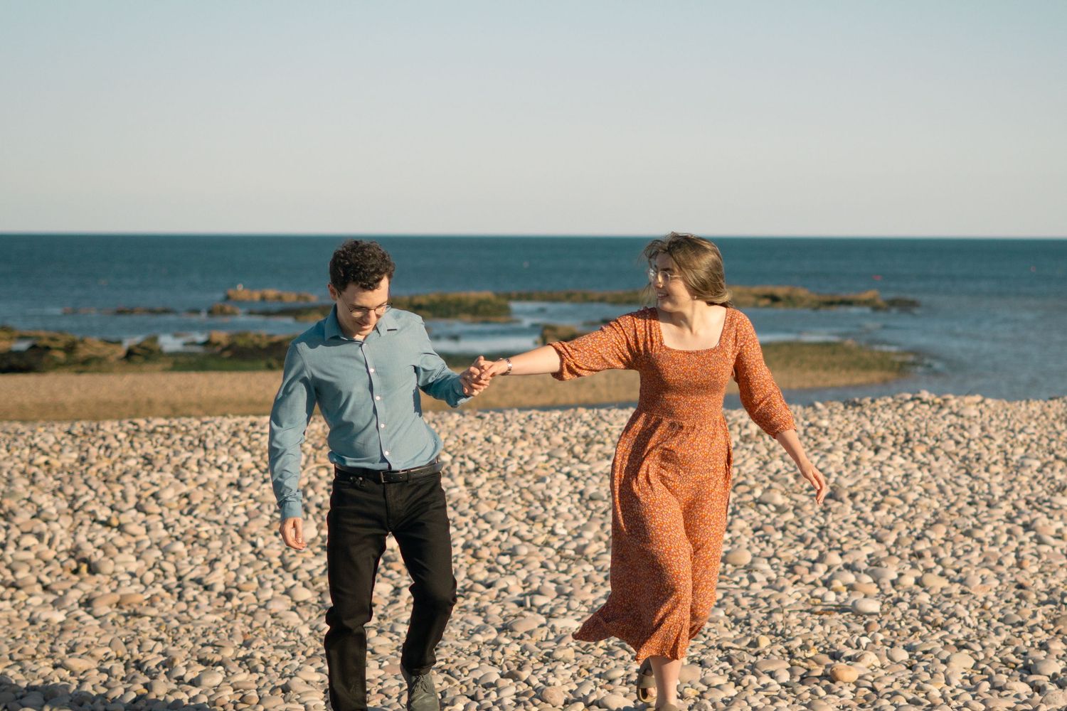 A couple walking together along the beach at Budleigh Salterton, Devon. The sea is turquoise behind them