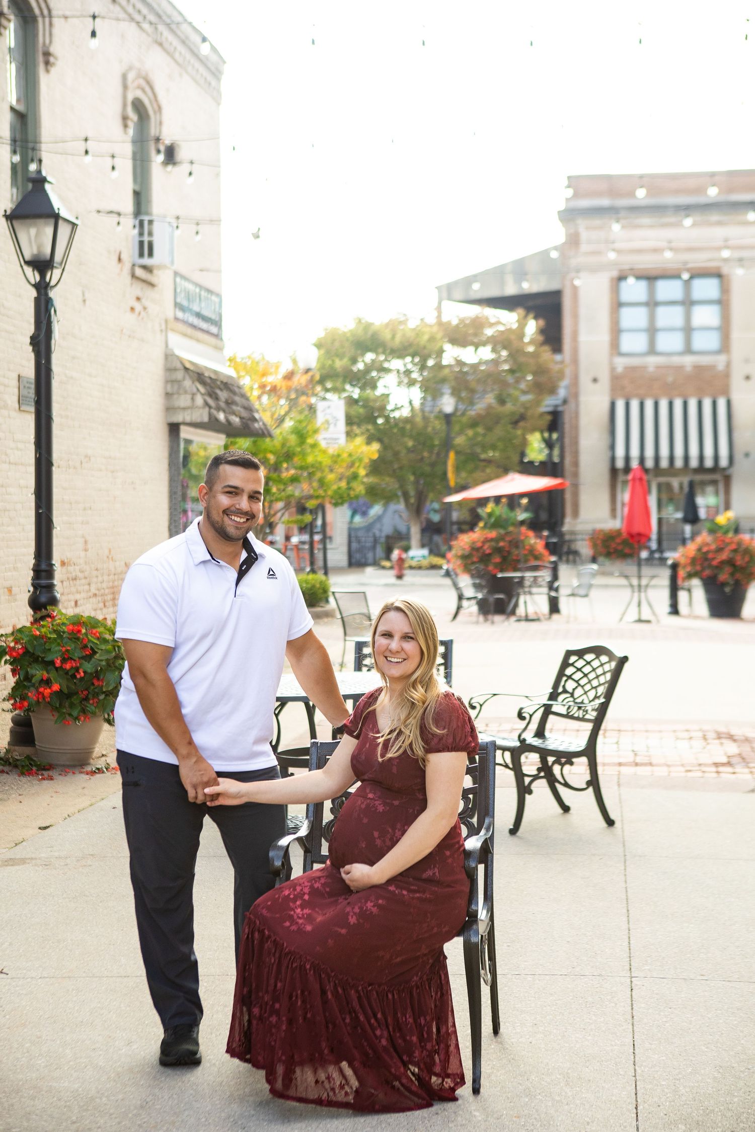 Outdoor maternity photos on urban plaza with couple in burgundy dress and white polo.