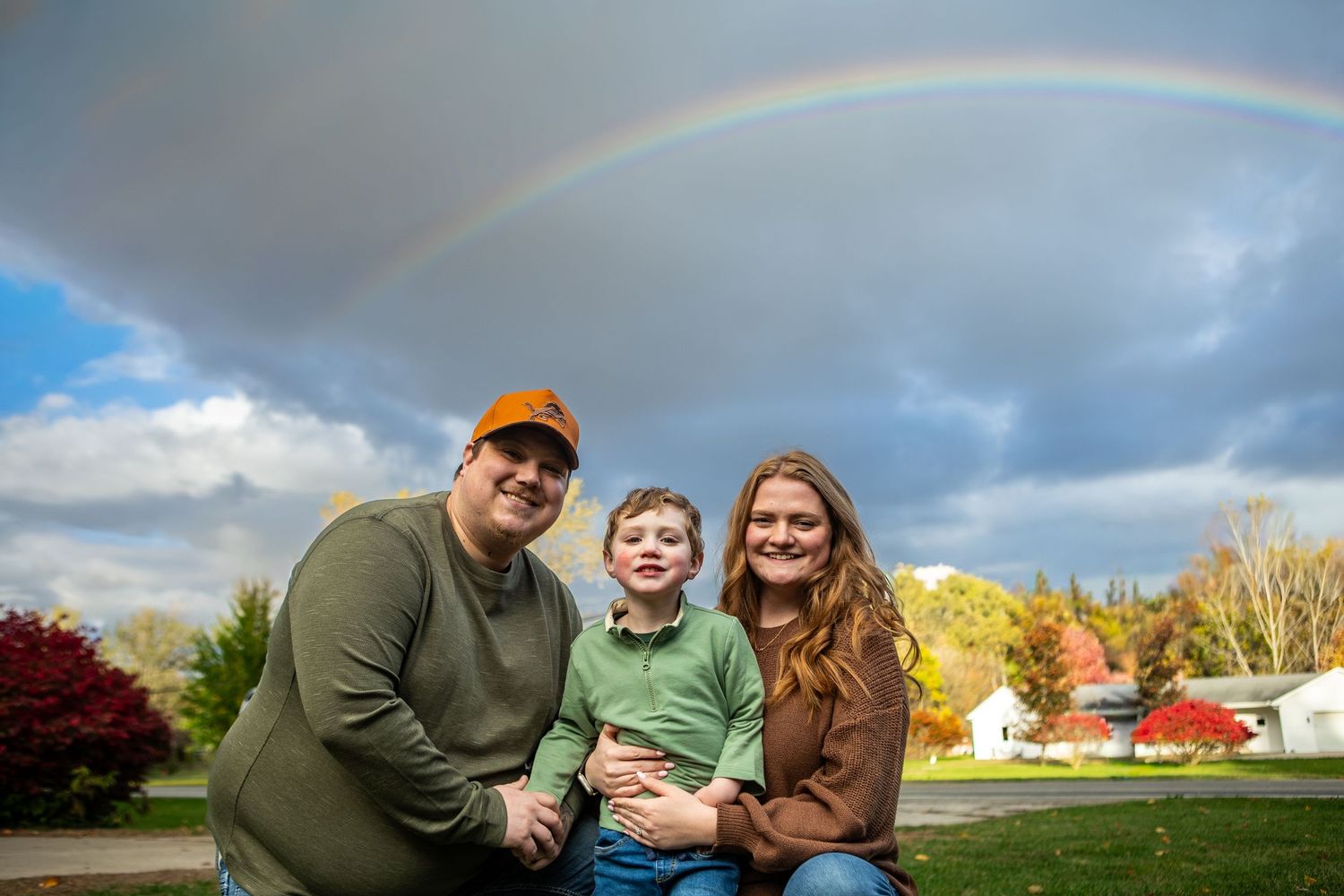 Family enjoying a beautiful rainbow in an open field during golden hour with dramatic clouds in the sky.