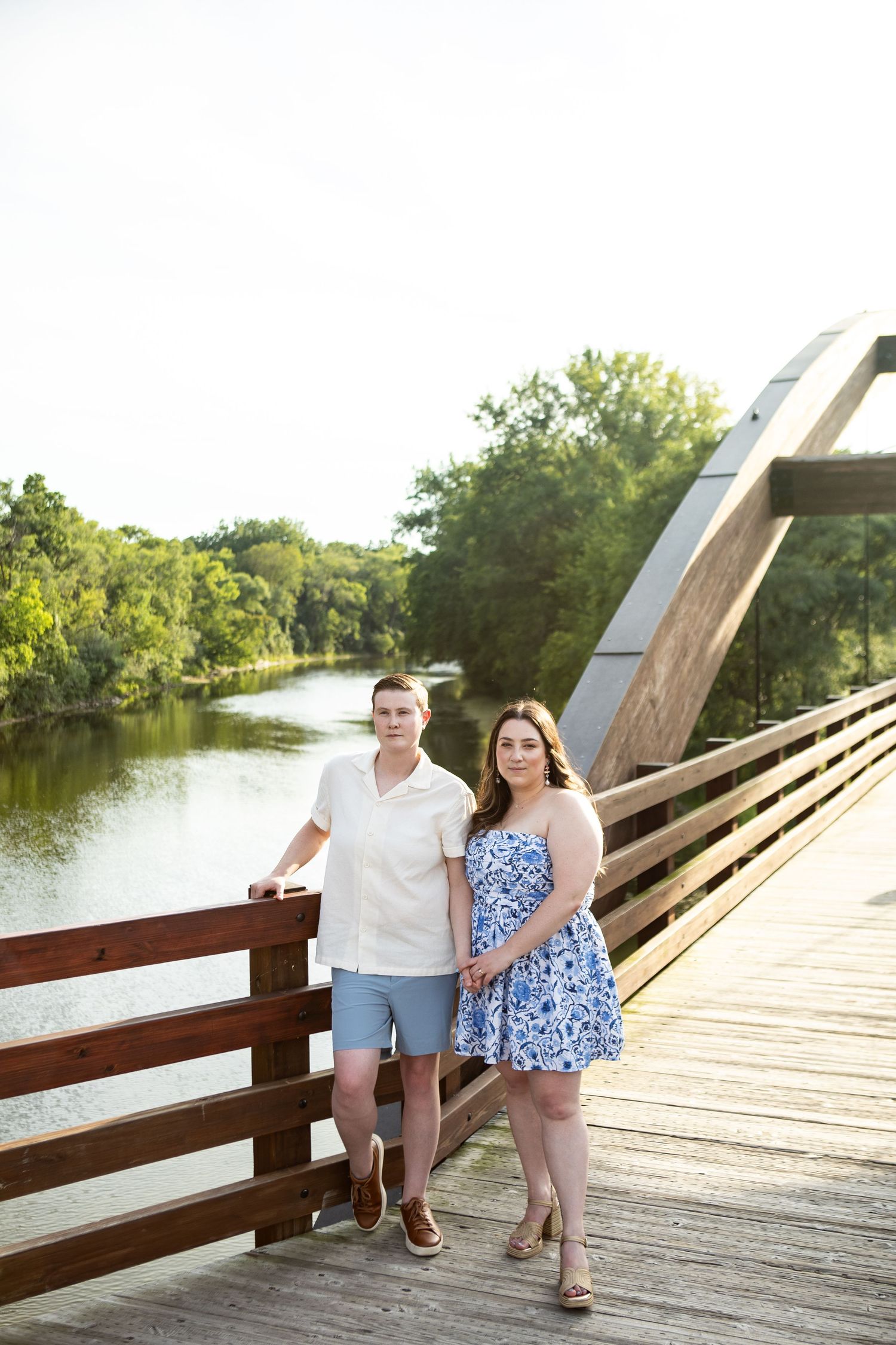 Couple poses together on a wooden bridge over water during sunset.