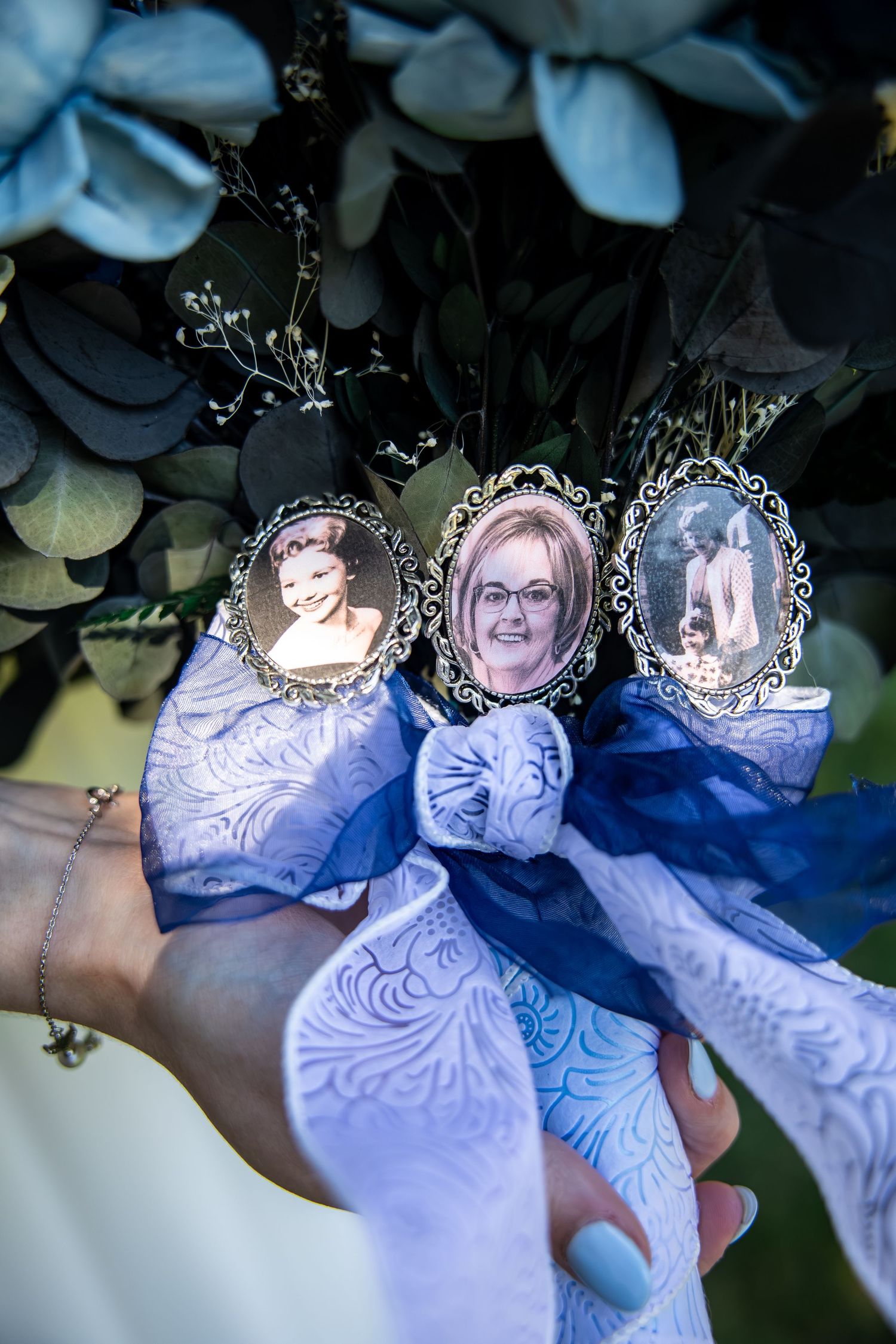 Bride holding a bouquet with silver framed memorial photo charms, lavender patterned ribbon, and eucalyptus greenery.