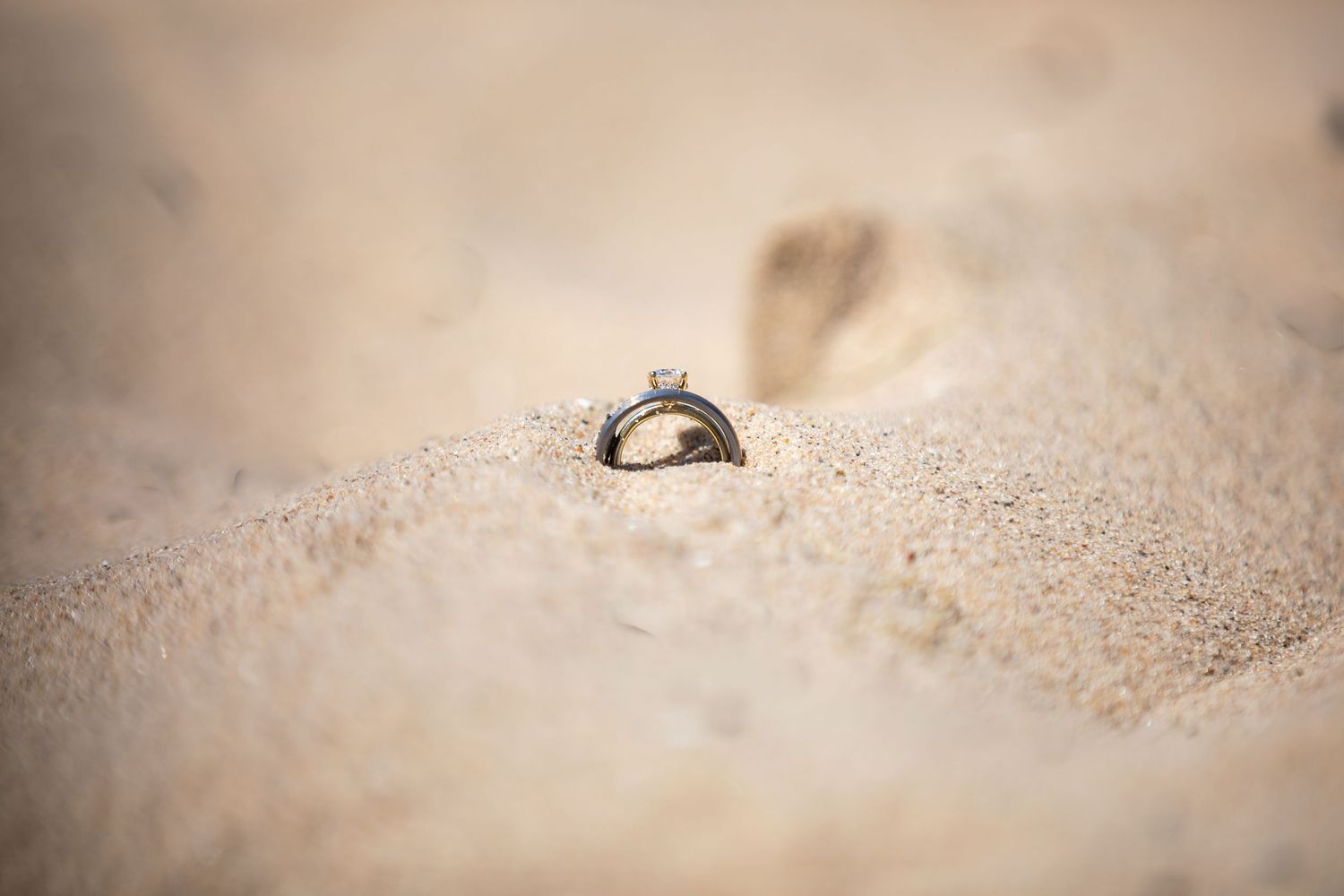 Two wedding rings nestled in soft sandy beach, symbolizing love and commitment in a romantic outdoor setting.