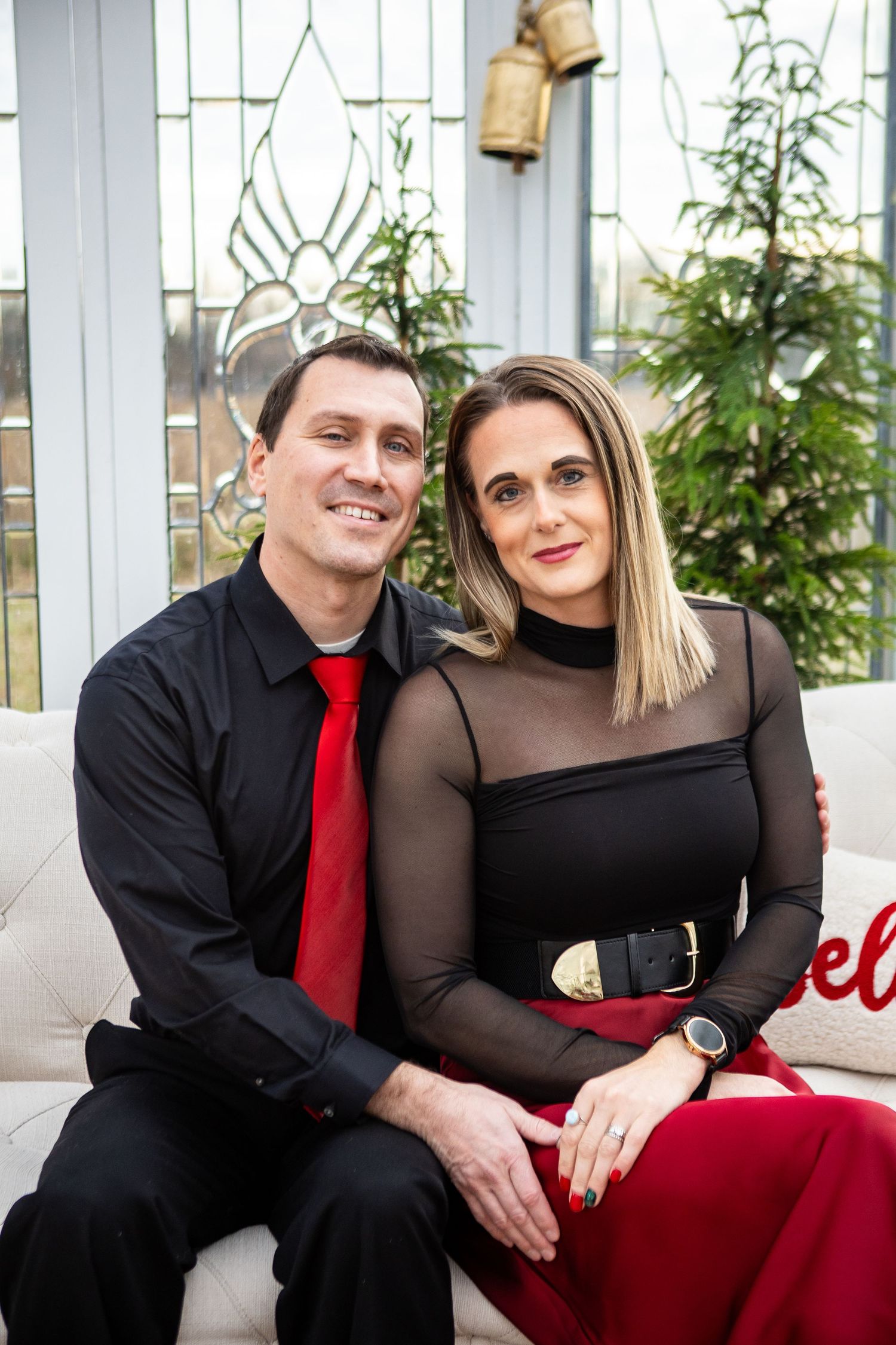 A couple in black and red formal attire pose together on a red couch in a romantic photo series.