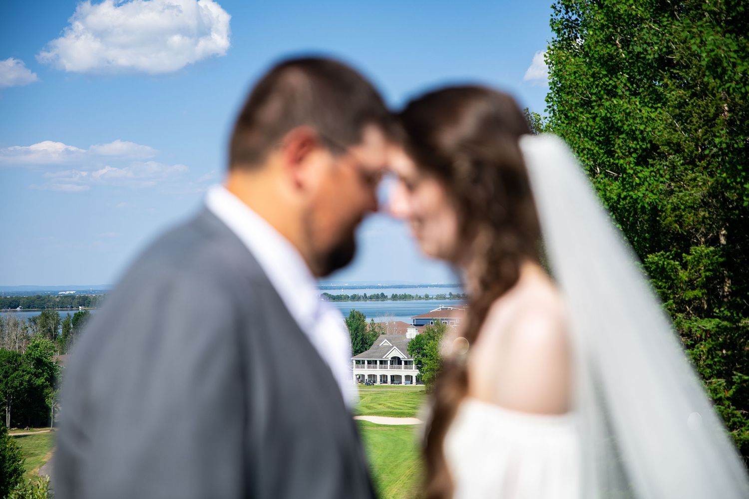 Bride and groom share an intimate moment outdoors with a scenic estate and blue sky in the background.