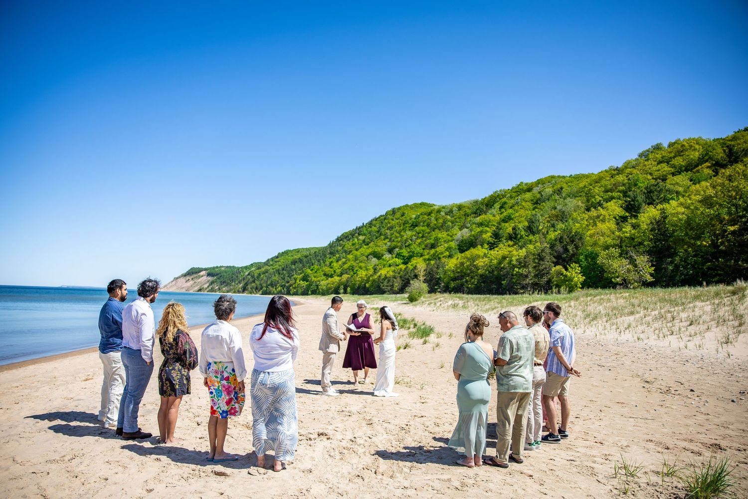 Small wedding ceremony on a sandy beach with lush green hills and blue sky backdrop.