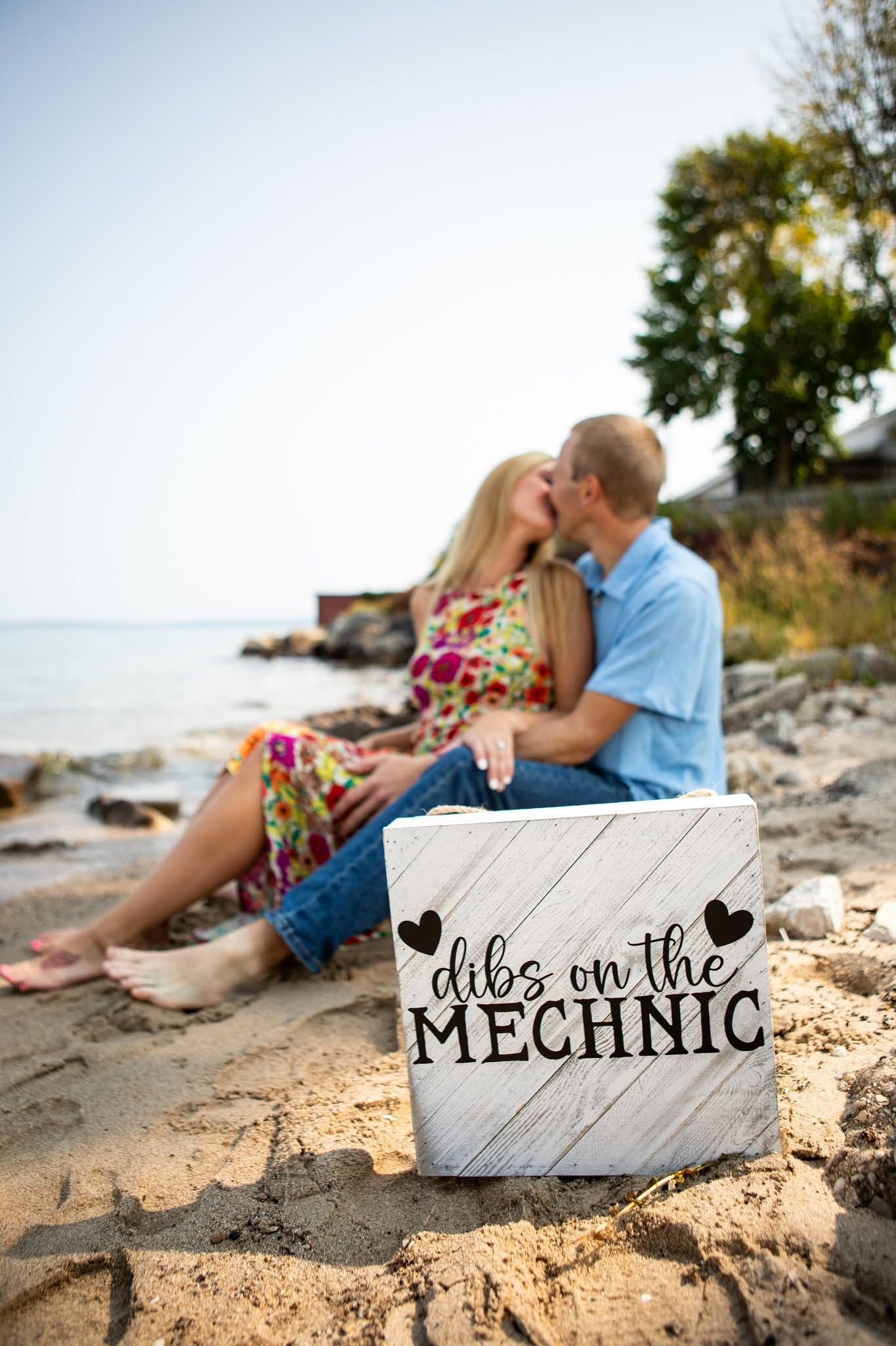Beach engagement photos with wooden signs reading 'Mechanic' displayed on sandy shore.