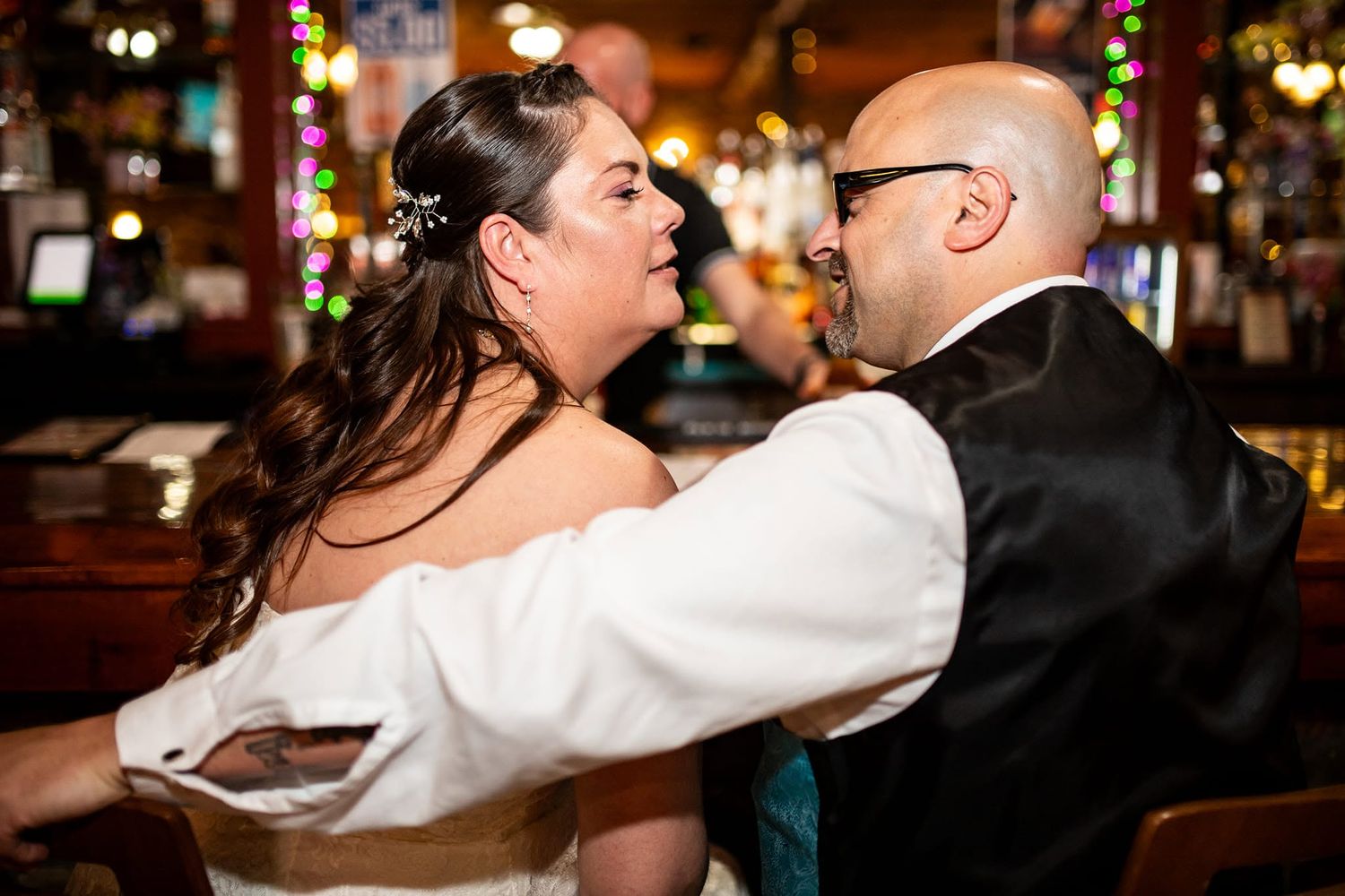 Couple sharing intimate dance moment at reception with festive lights in background.