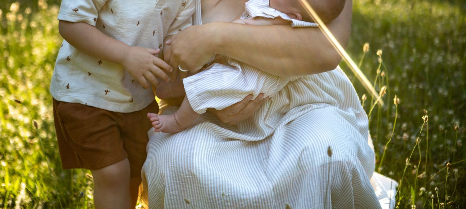 Intimate family moment captured in warm sunlight with natural outdoor backdrop.