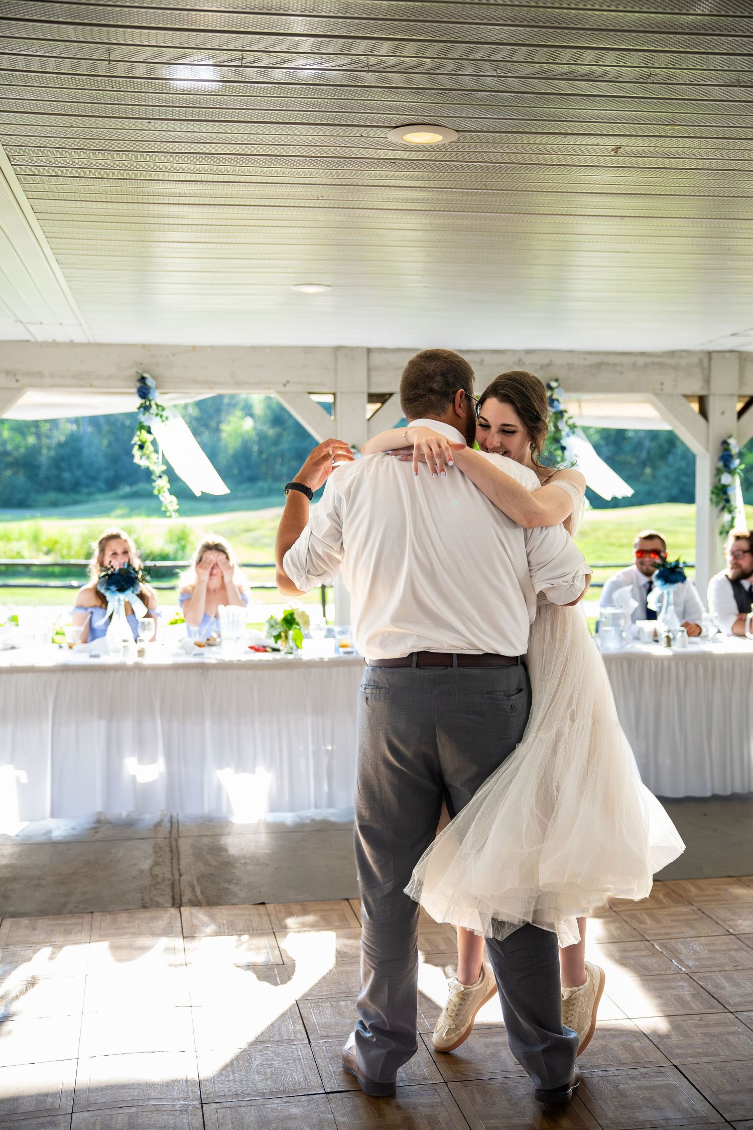 Bride and groom share their first dance at an outdoor wedding reception under a white pavilion.