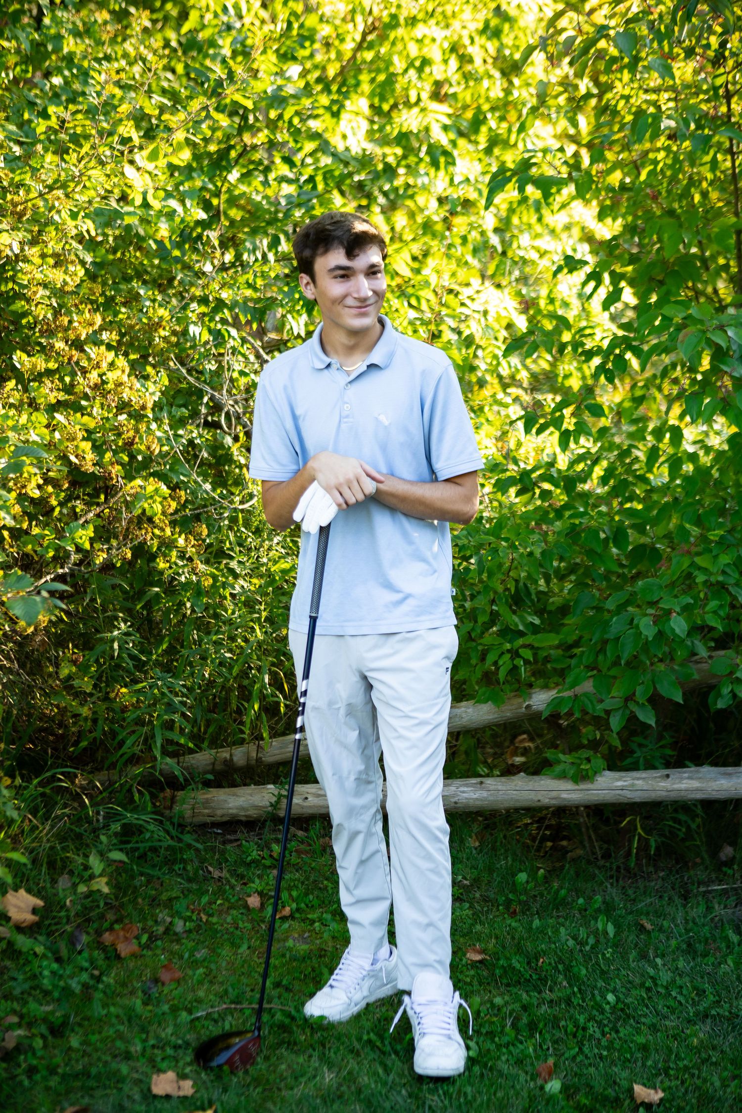 A person in white coveralls stands in a lush garden setting with bright green foliage and golden sunlight.