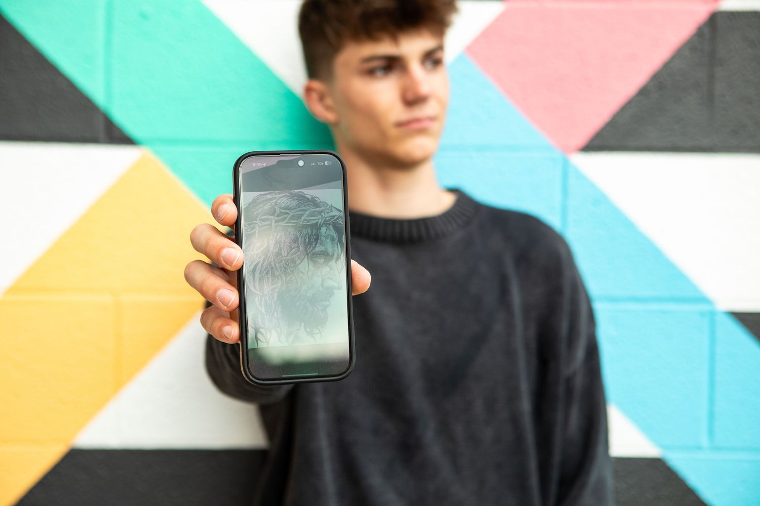 A person holds up a smartphone with a colorful geometric wall in the background.