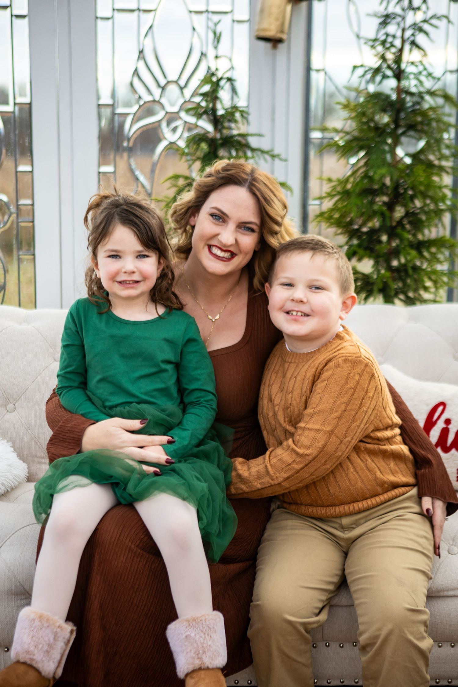 Family wearing coordinated brown and green outfits poses together in front of white window backdrop.