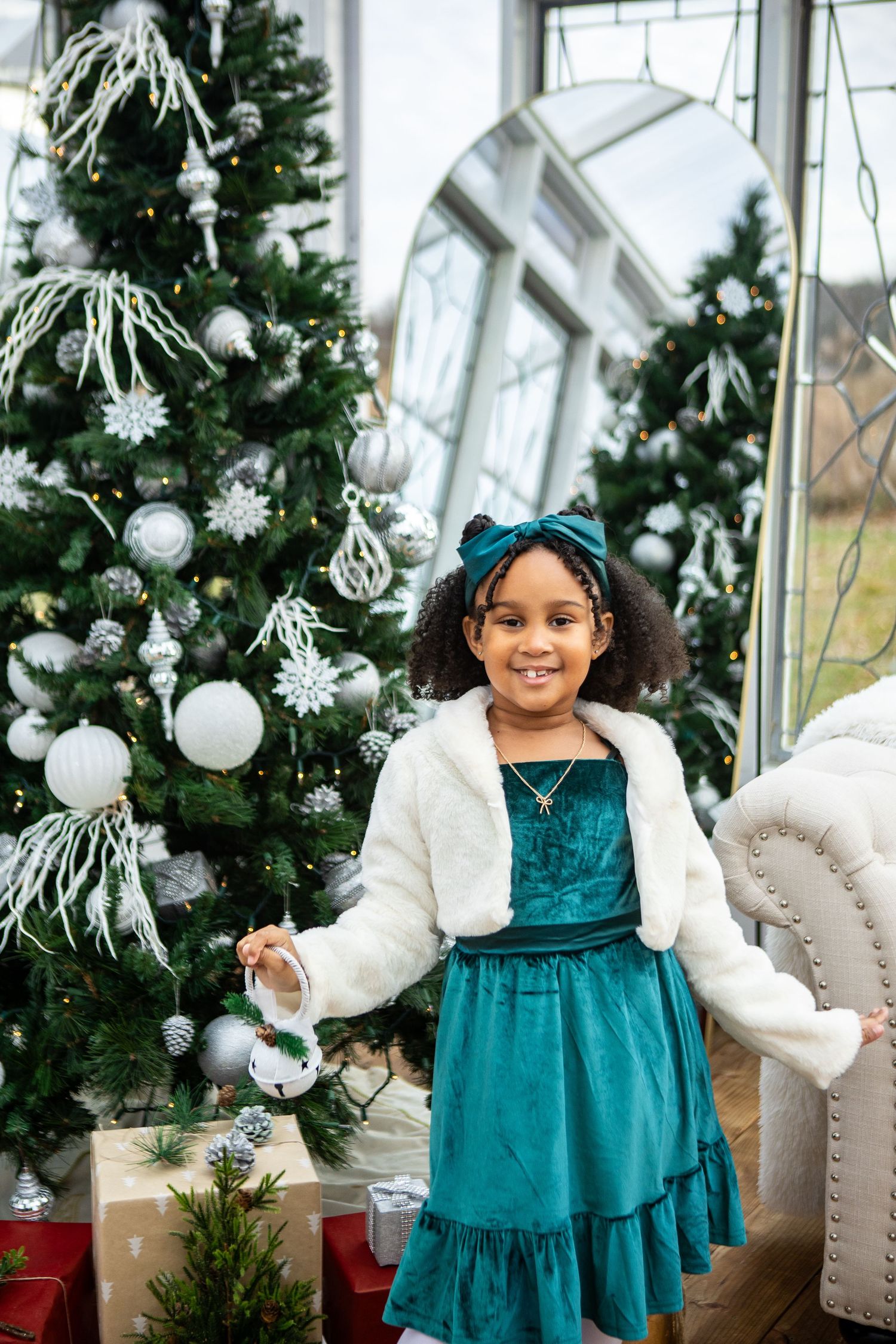 A festive holiday scene with evergreen trees decorated in white ornaments and a teal velvet dress.