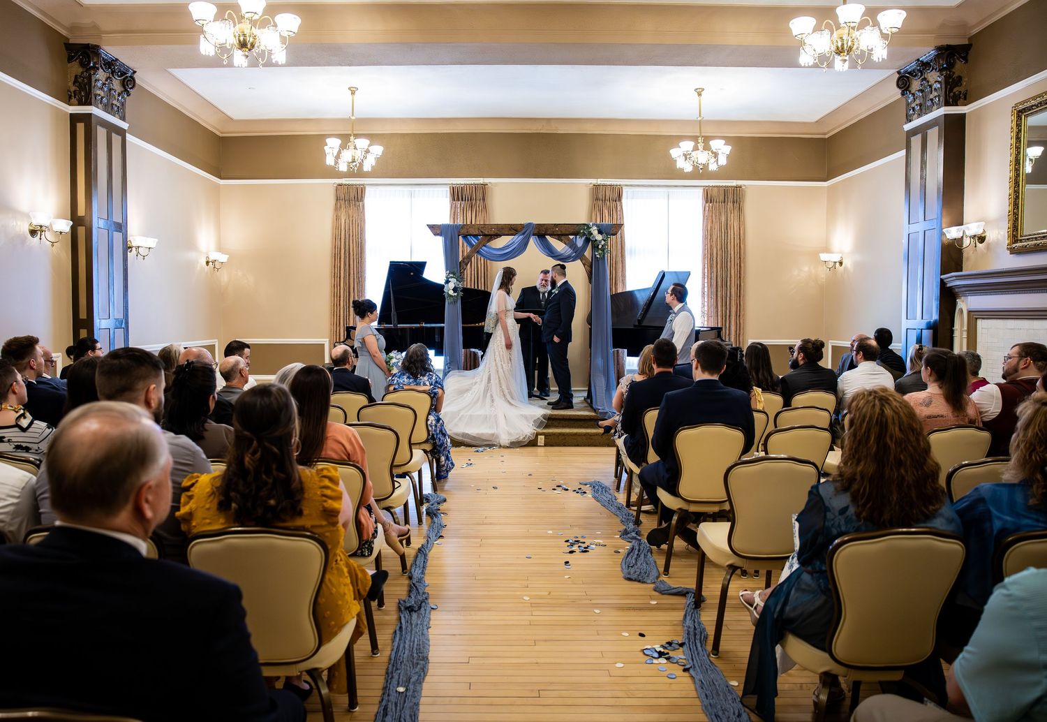 Elegant wedding ceremony in a grand ballroom with guests seated in rows facing the couple at the altar.