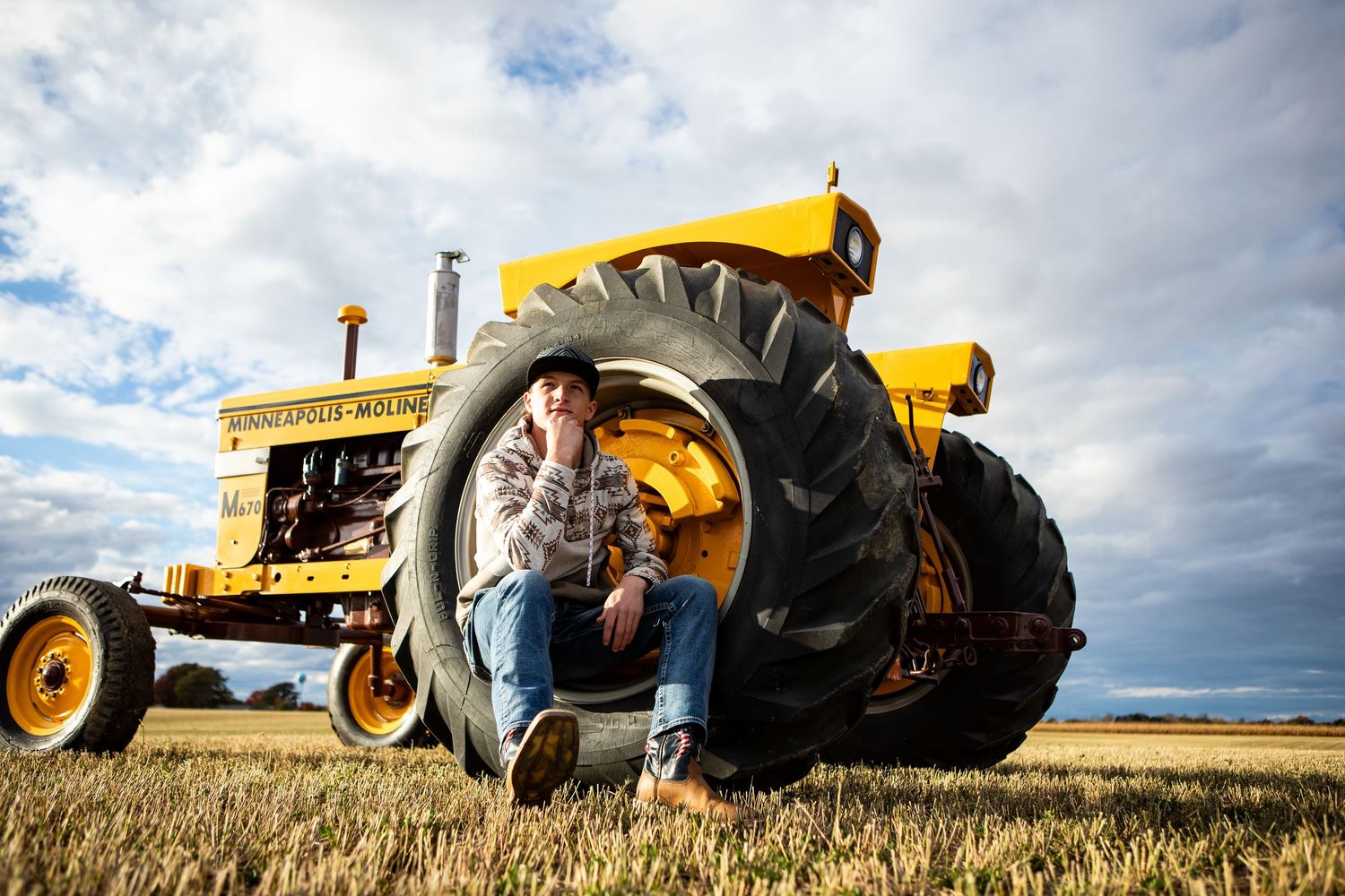 Vintage yellow tractors lined up in wheat field under cloudy sky.